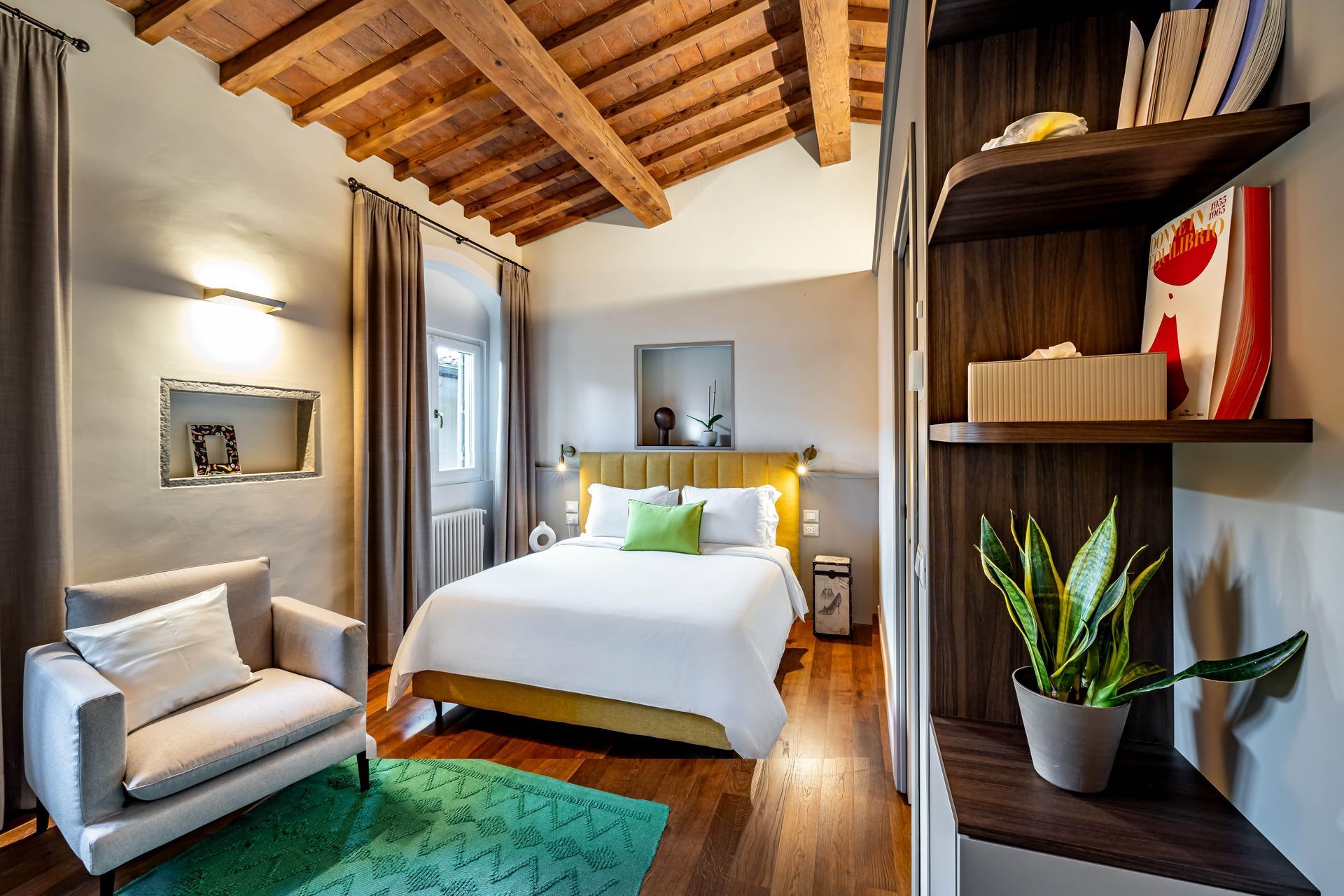 Le Torri by Dimora Collection: Cozy bedroom with exposed wood ceiling, bed, armchair, desk, and large windows