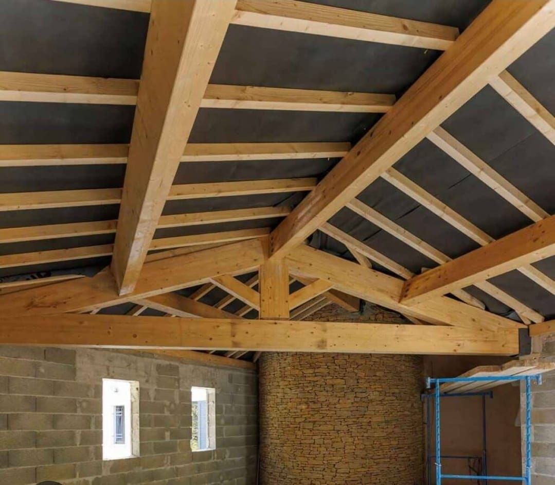 Intérieur avec charpente apparente en bois au-dessus de murs en briques brutes.