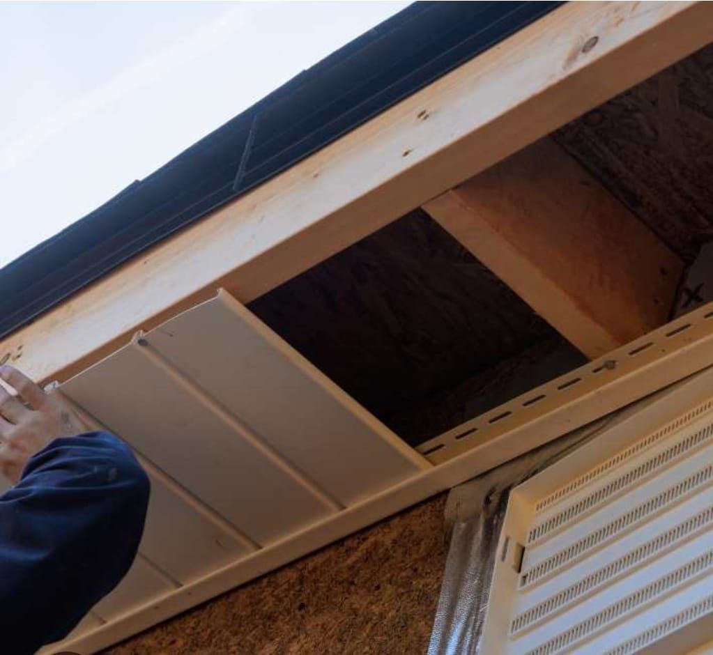Une personne installe des panneaux de sous-toiture blancs sous l'avant-toit d'une maison à l'extérieur.
