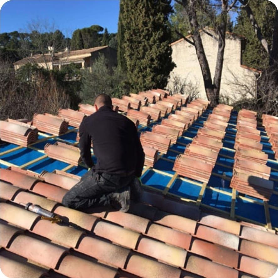Ouvrier posant des tuiles en terre cuite sur un toit sous un ciel bleu dégagé