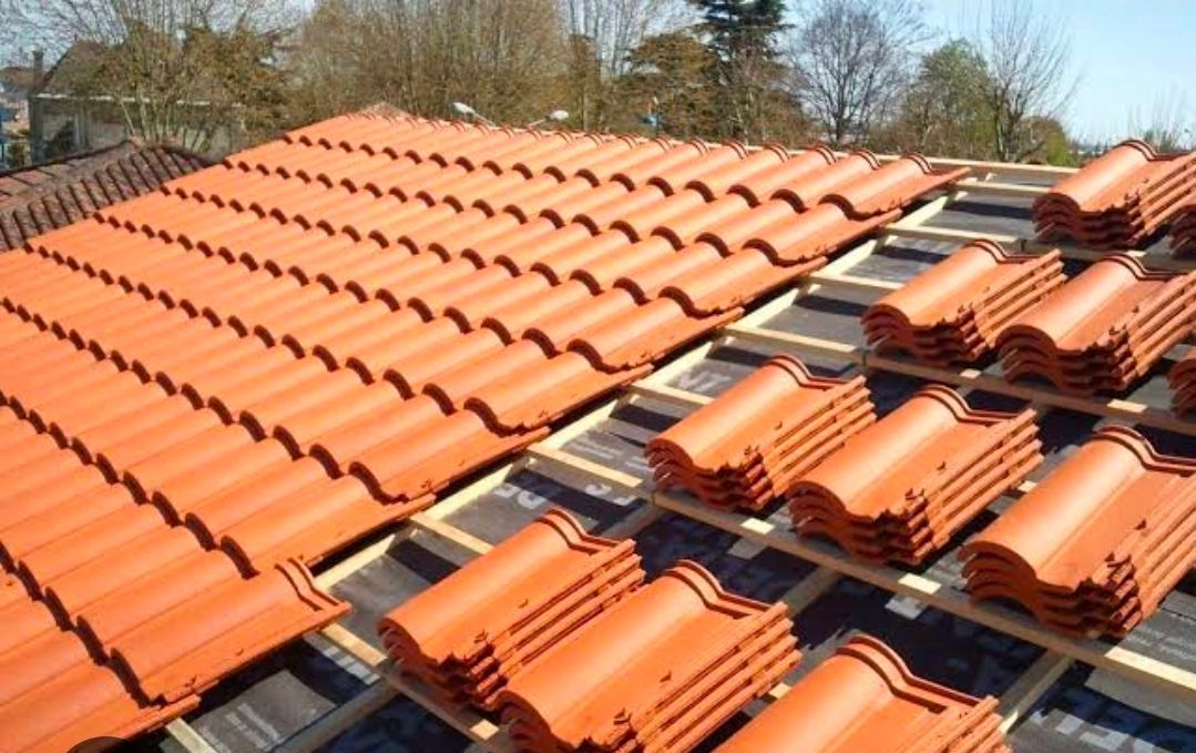 Pose de tuiles en terre cuite sur une maison, les tuiles étant empilées sur le côté droit.