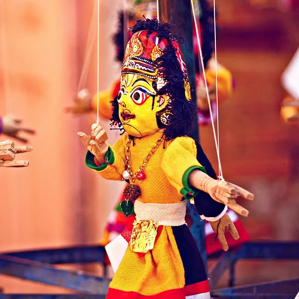 Bunte Marionette mit erhobenen Armen, in gelber und roter Kleidung, vor einem warmen, verschwommenen Hintergrund