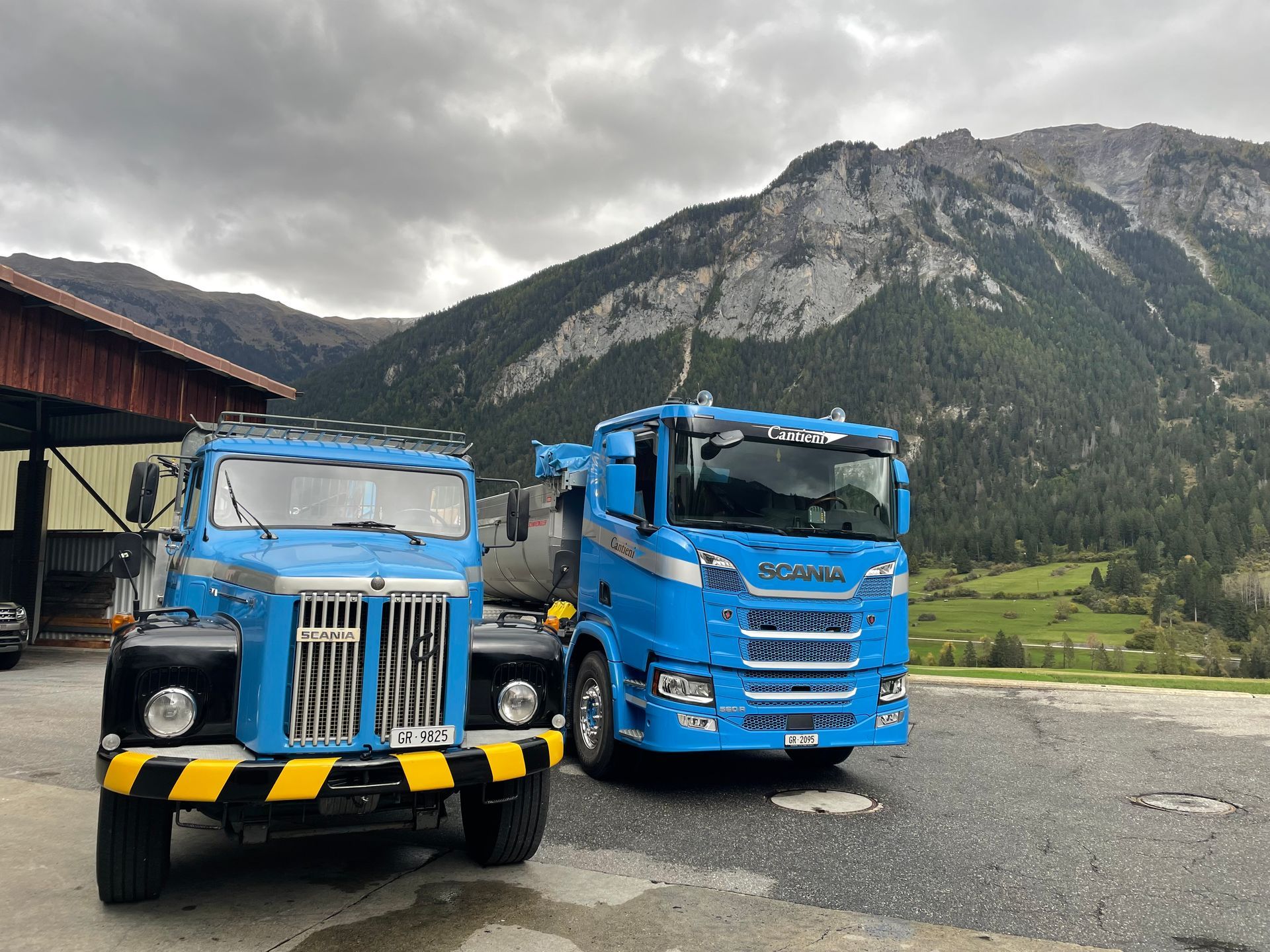 Zwei blaue Lastwagen parken nebeneinander vor einem Berg.
