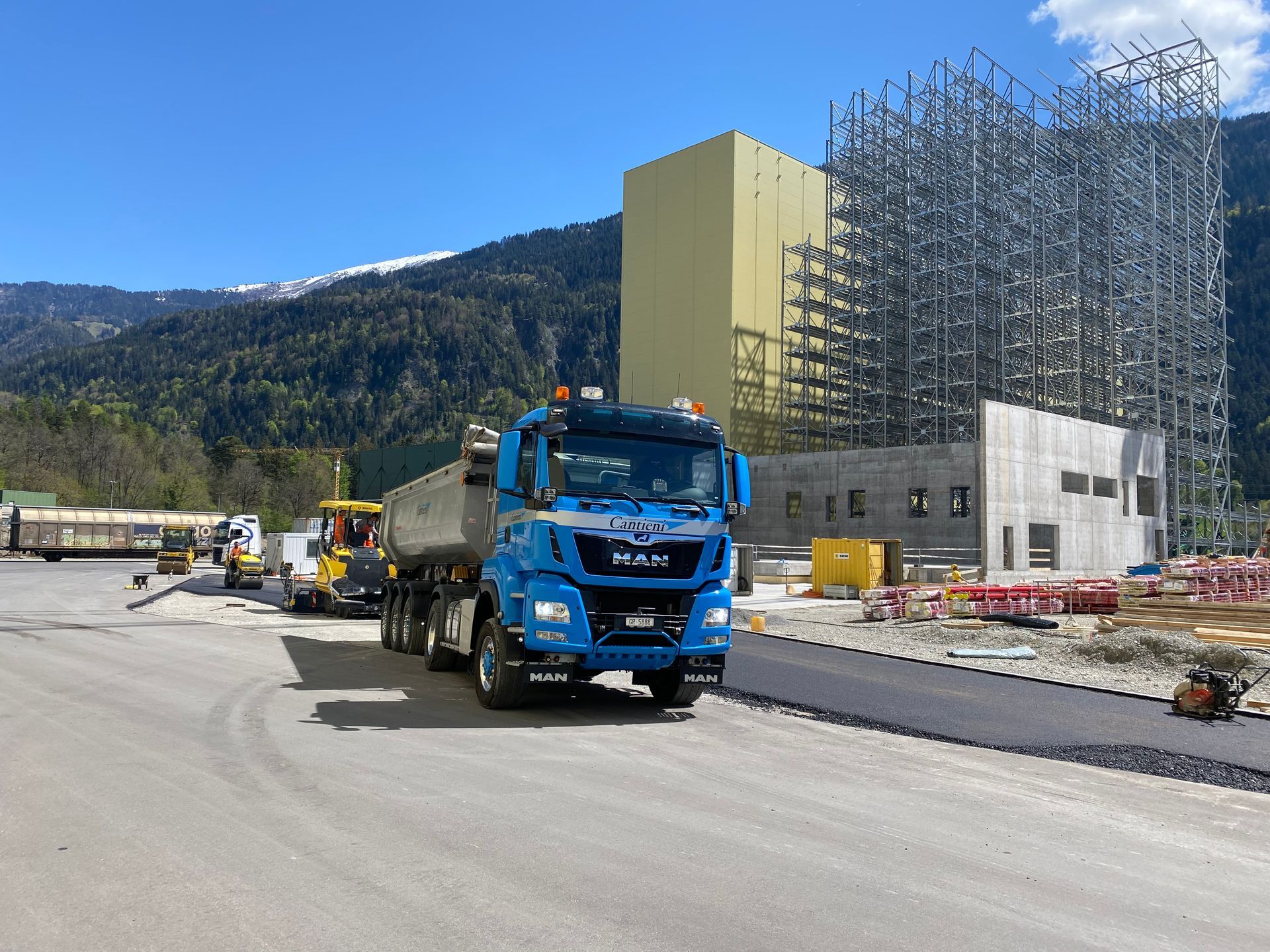 Ein Lastwagen fährt auf einer Straße vor einem im Bau befindlichen Gebäude entlang.