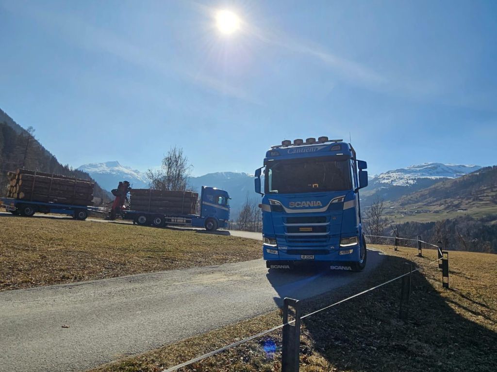 Ein blauer Lastwagen fährt eine Straße entlang, im Hintergrund sind Berge zu sehen.
