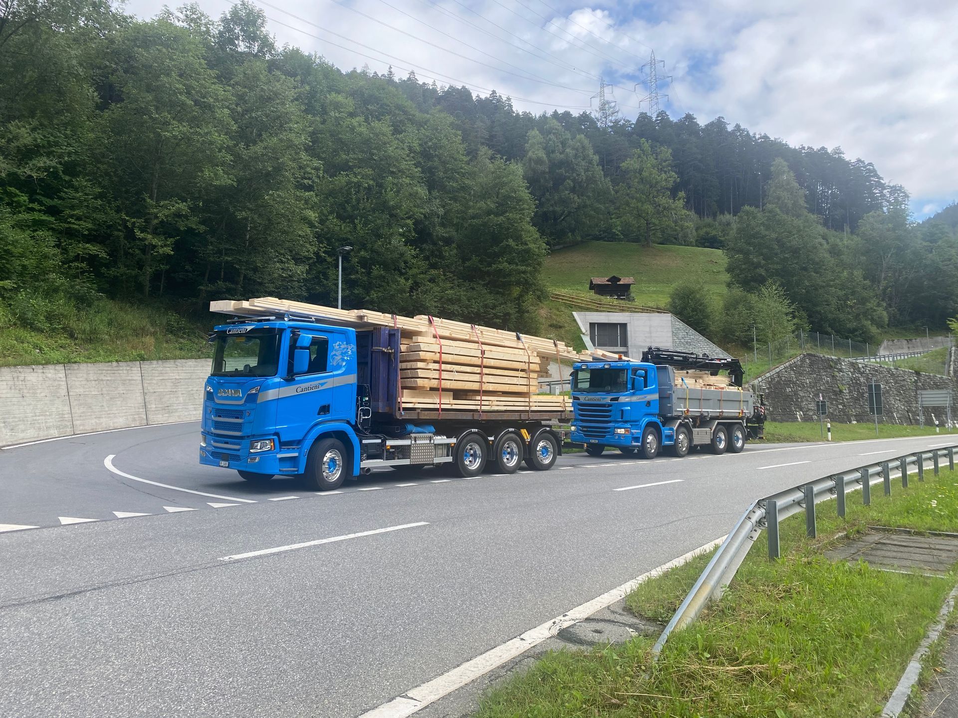 Zwei blaue Lastwagen fahren mit Holzpaletten beladen eine Straße entlang.