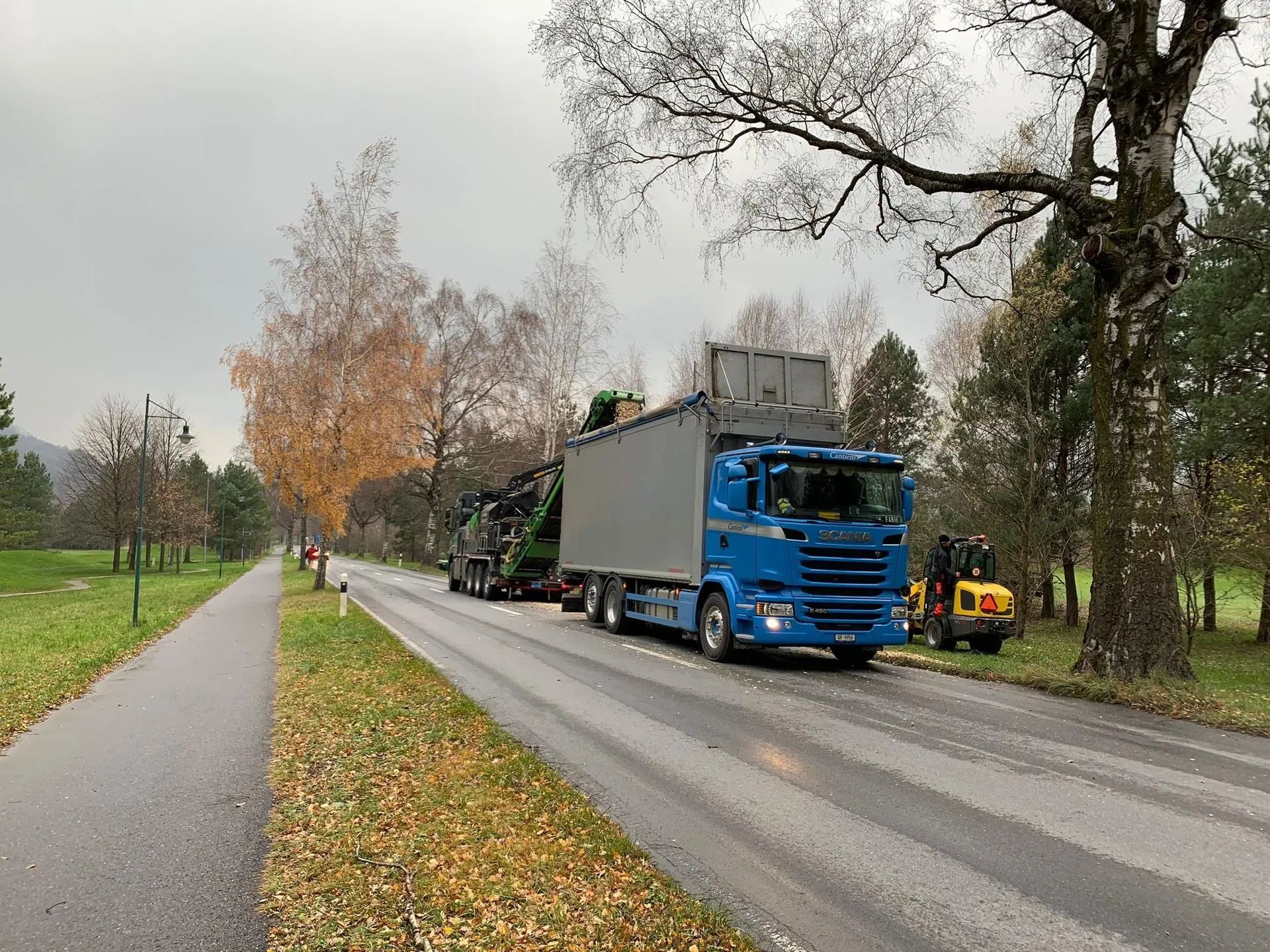 Ein blauer Lastwagen fährt eine Straße neben einem Park entlang.