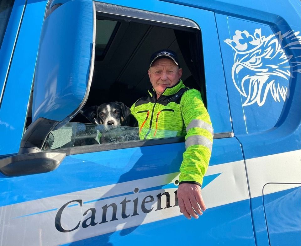 Ein Mann und ein Hund sitzen auf dem Fahrersitz eines blauen Lastwagens.