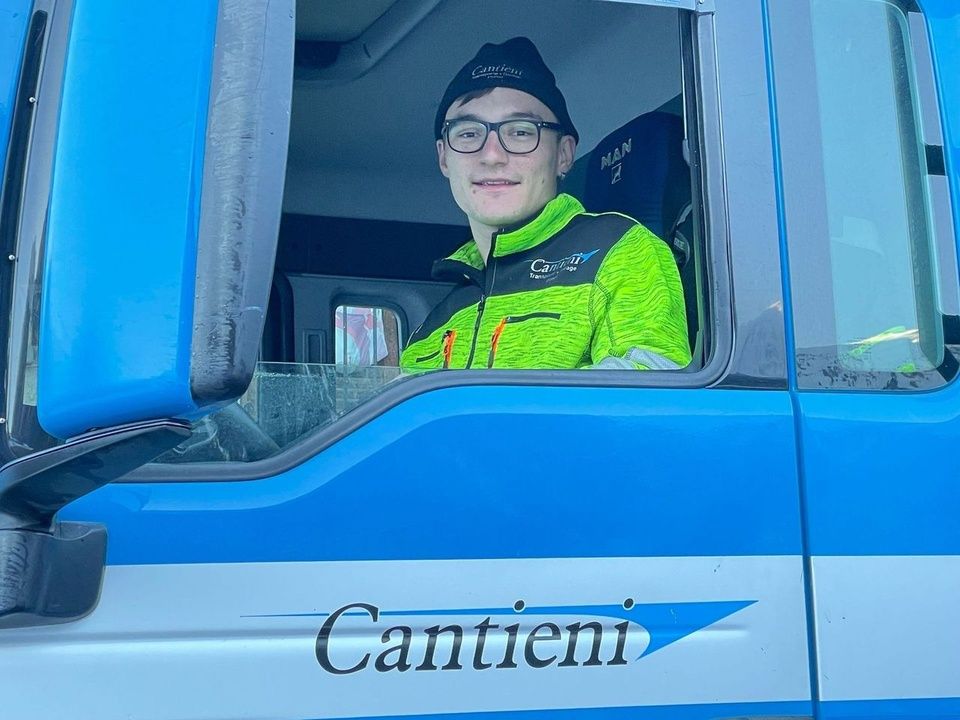 Ein Mann sitzt auf dem Fahrersitz eines blau-weißen Lastwagens.