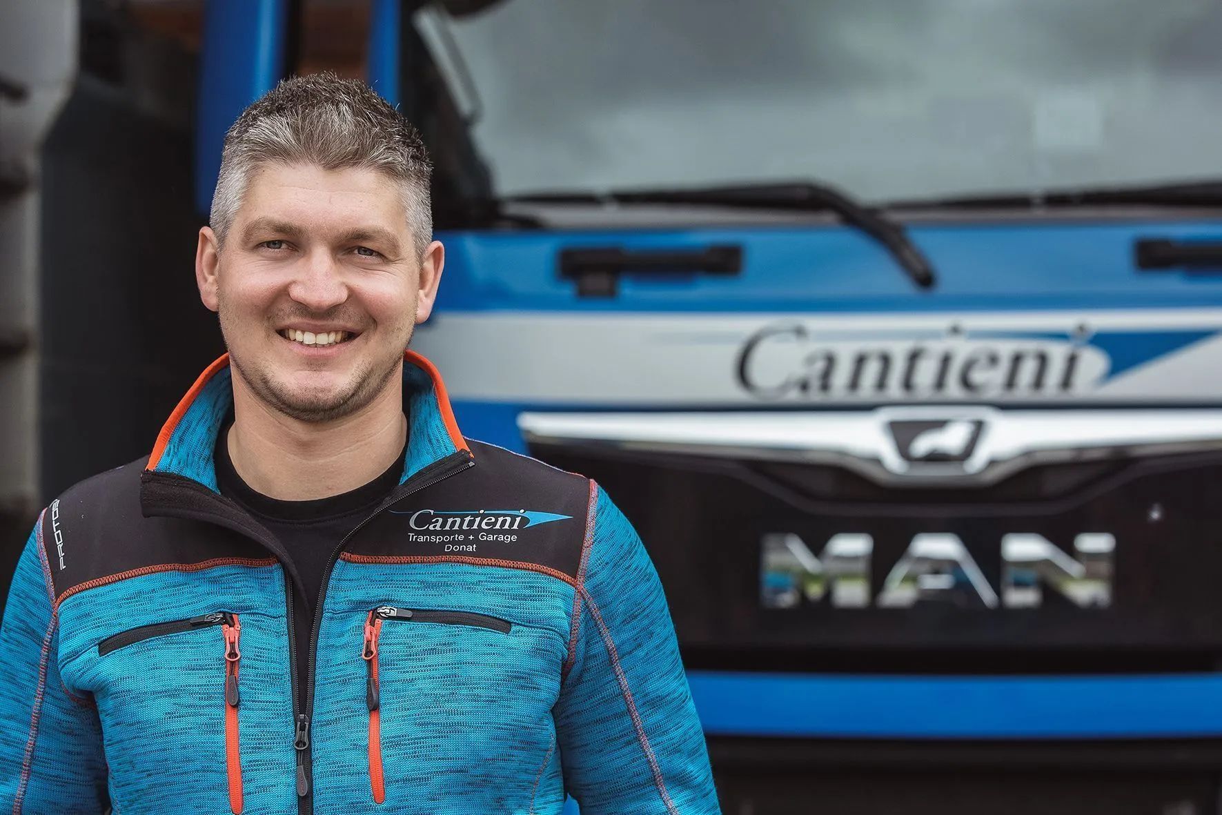 Ein Mann in einer blauen Jacke steht vor einem blauen Lastwagen.