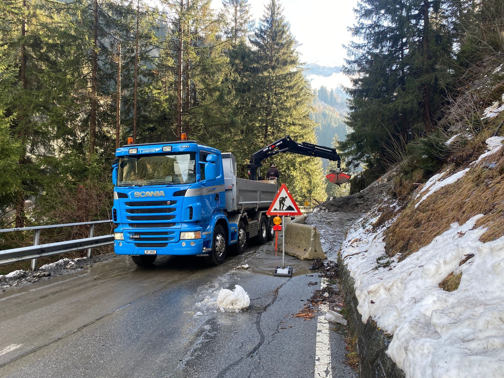 Ein blauer Lastwagen fährt eine verschneite Straße entlang.