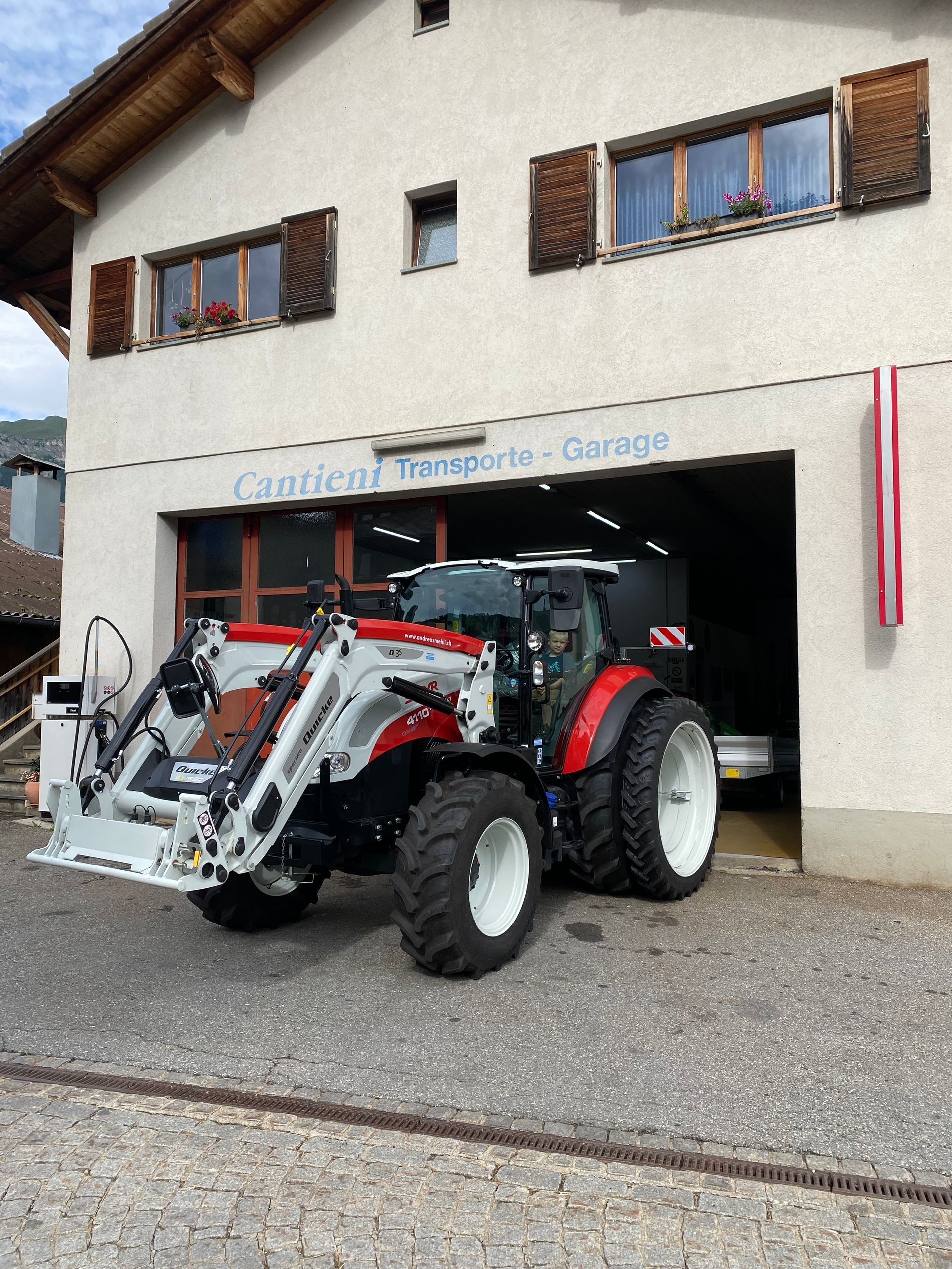Vor einem Gebäude parkt ein rot-weißer Traktor.