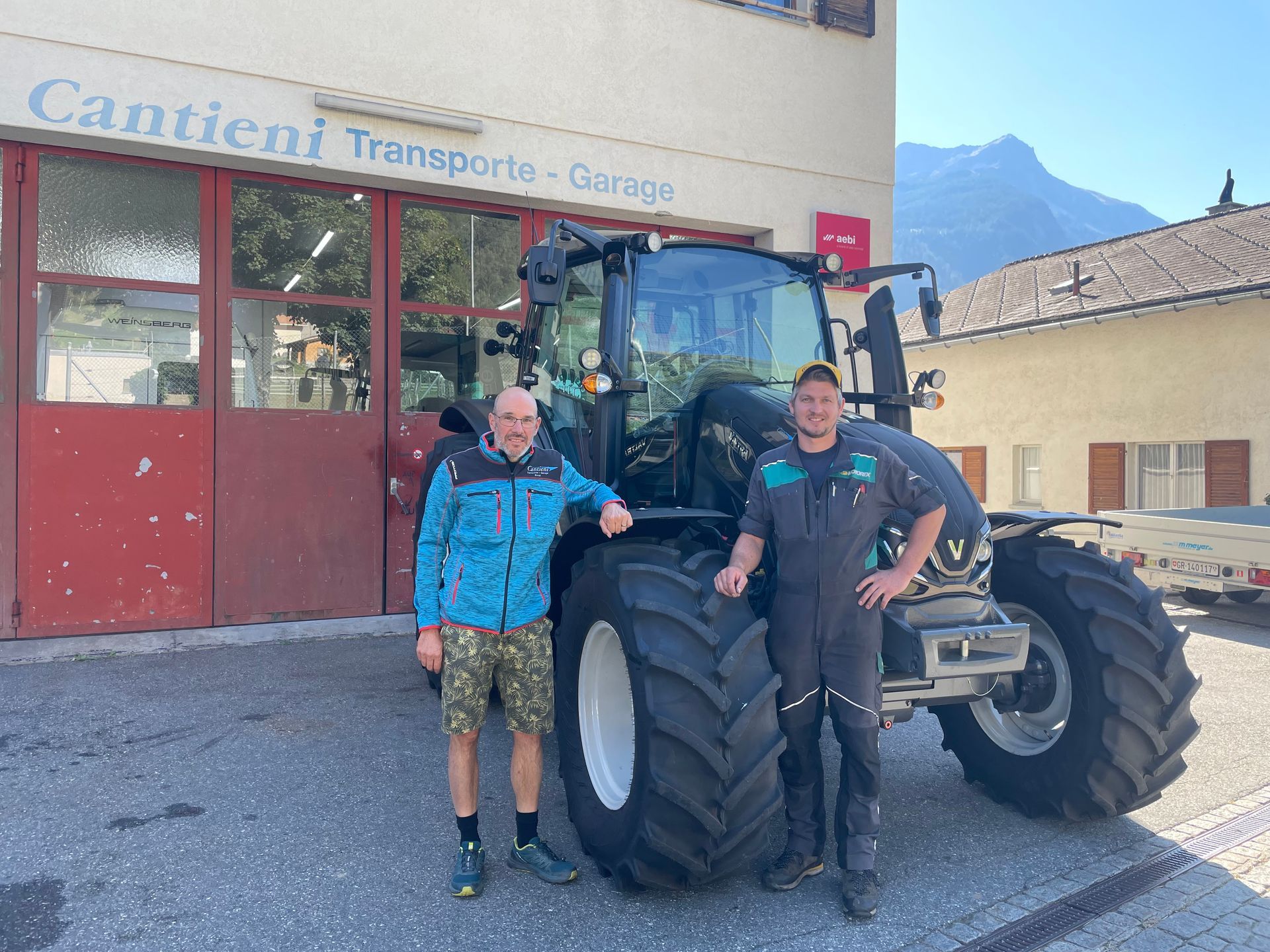 Zwei Männer stehen neben einem Traktor vor einem Gebäude.