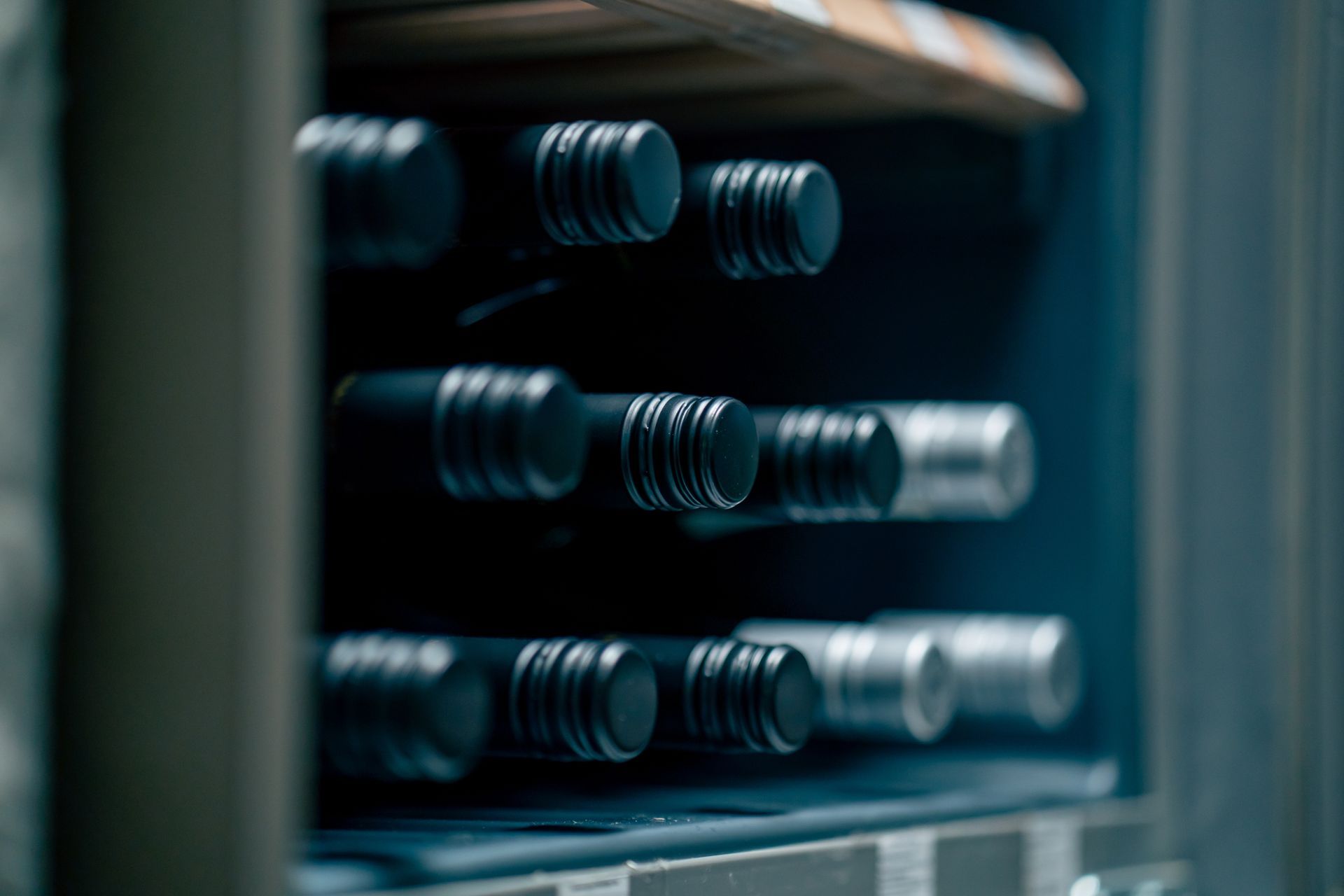 Une personne tenant un verre de vin rouge l'examine dans une cave à vin. Des bouteilles sont alignées sur des étagères à l'arrière-plan.