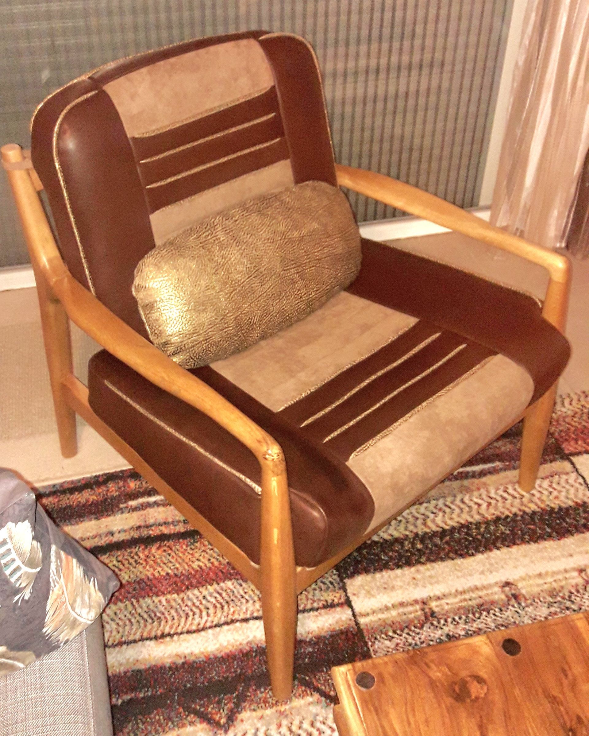 Fauteuil rembourré marron et crème avec coussin lombaire sur un tapis rayé dans un salon.