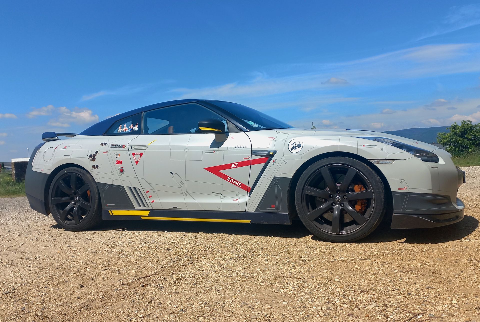 Voiture de sport argentée à jantes noires garée sur un chemin de gravier sous un ciel bleu