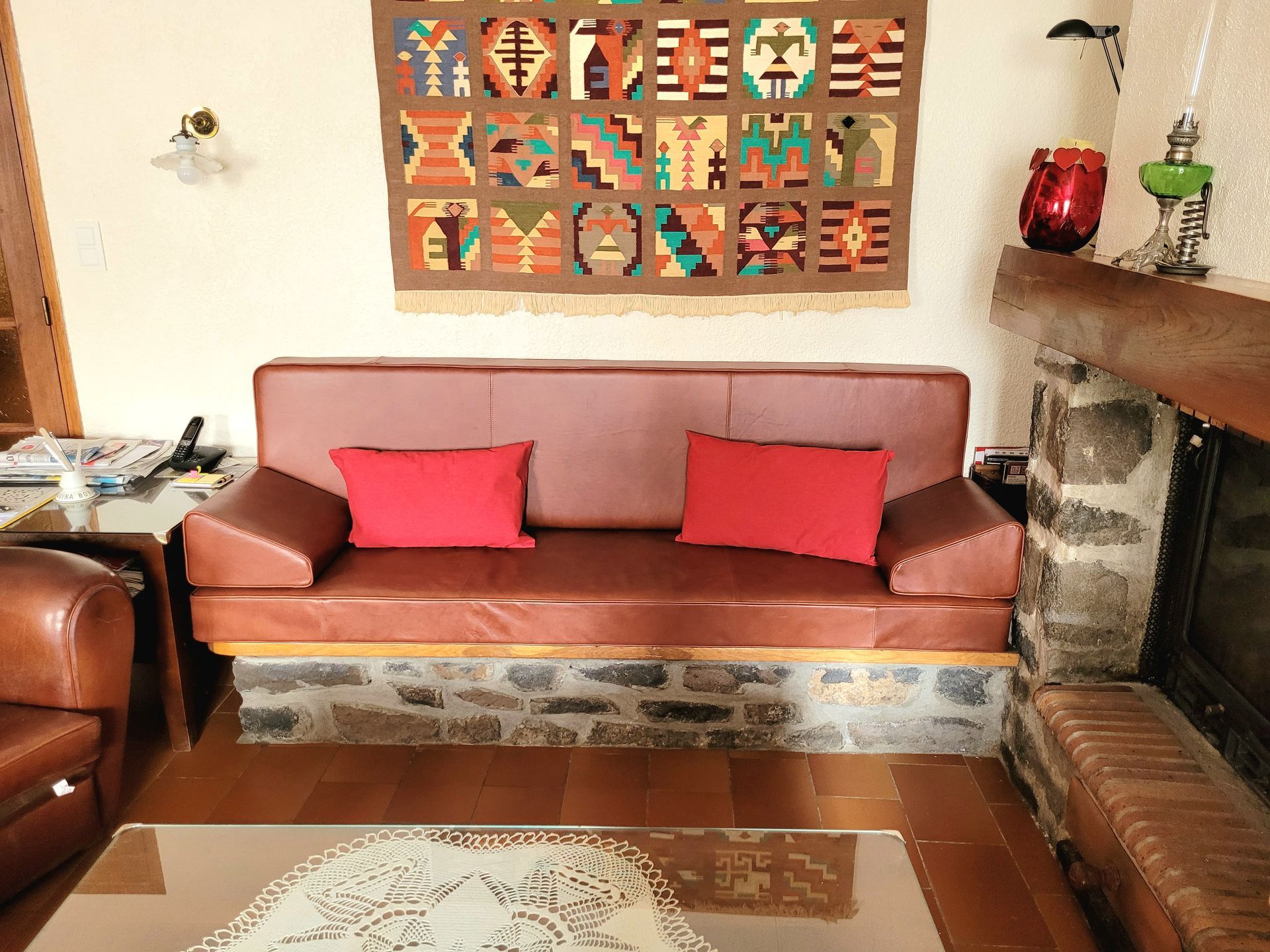 Salon avec un canapé marron, des coussins rouges, une cheminée en pierre et des tableaux colorés.