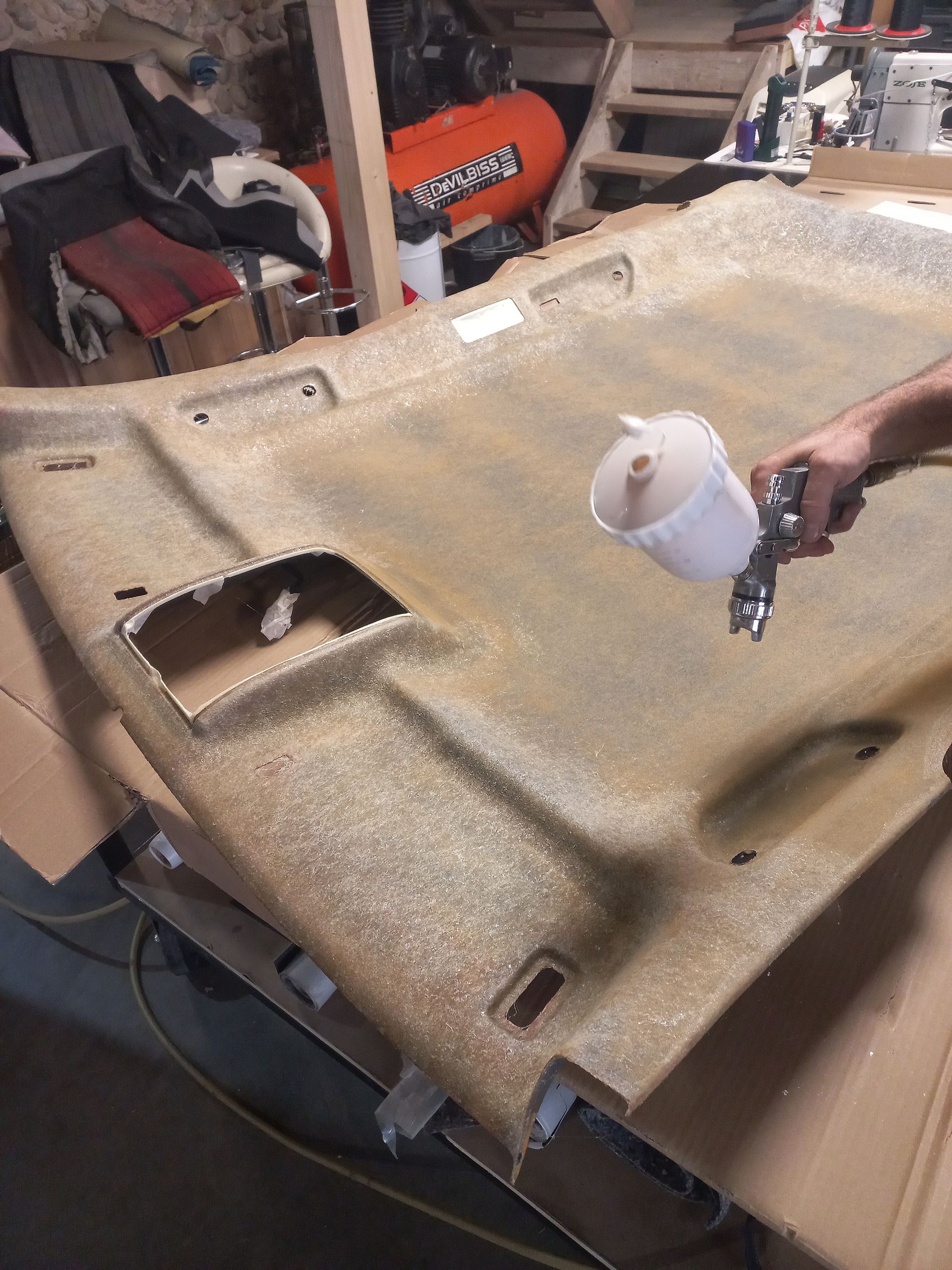 Une personne pulvérise de la mousse de rembourrage beige dans un atelier à l'aide d'un pistolet à peinture.