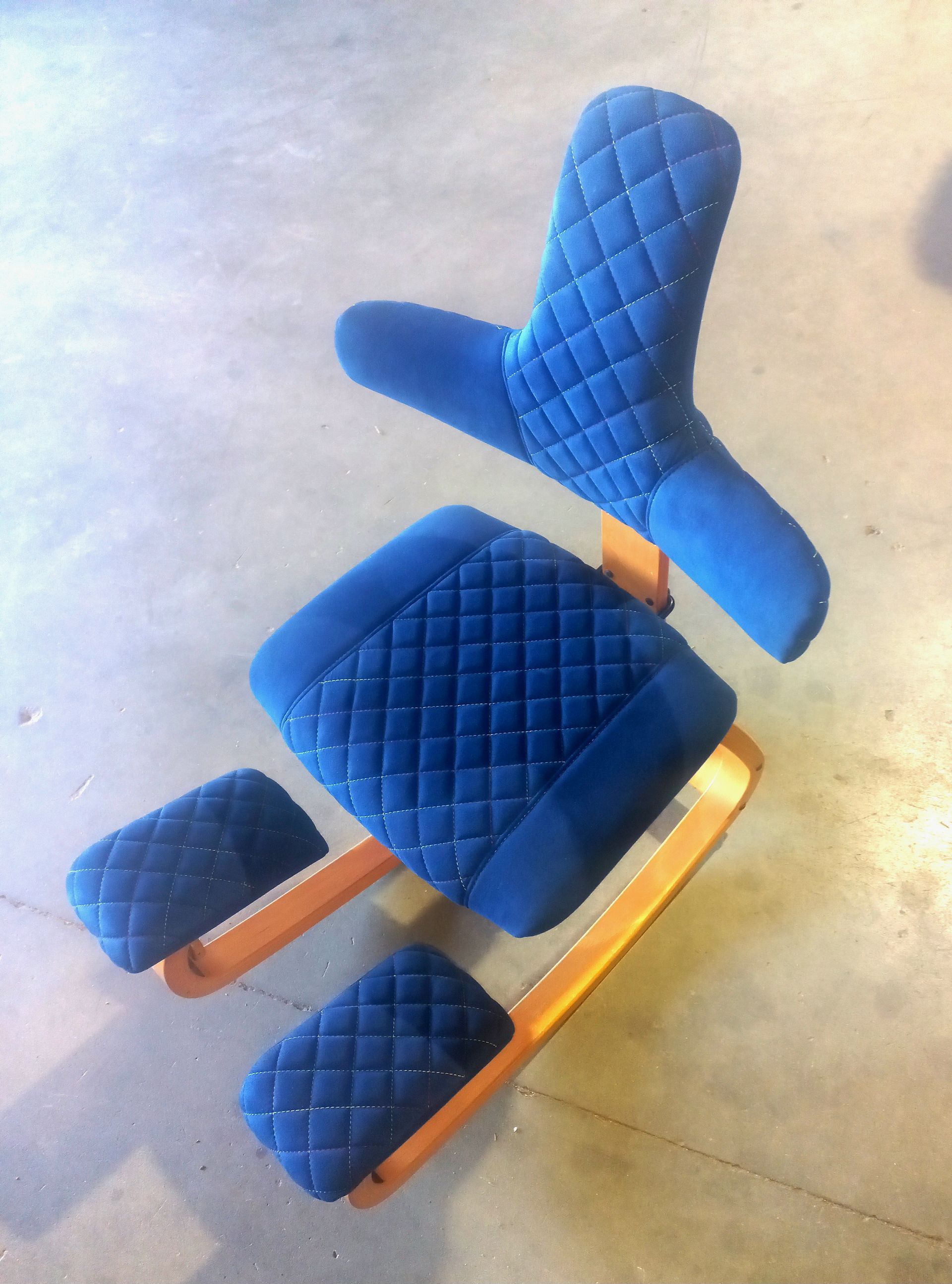 Chaise ergonomique matelassée bleue avec structure et repose-pieds orange sur un sol clair