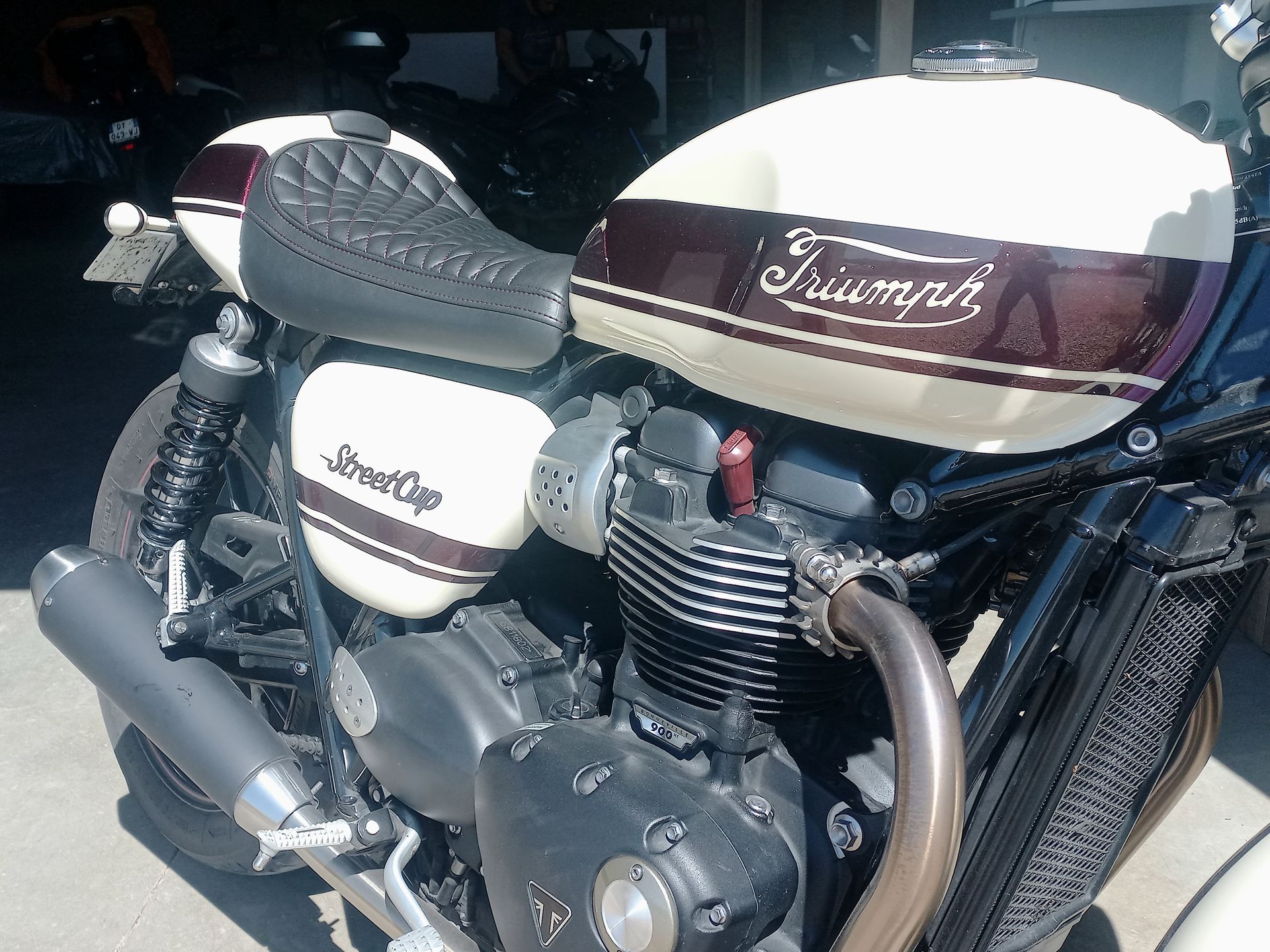 Moto Triumph customisée avec réservoir blanc et bordeaux et échappement chromé, garée dans un garage