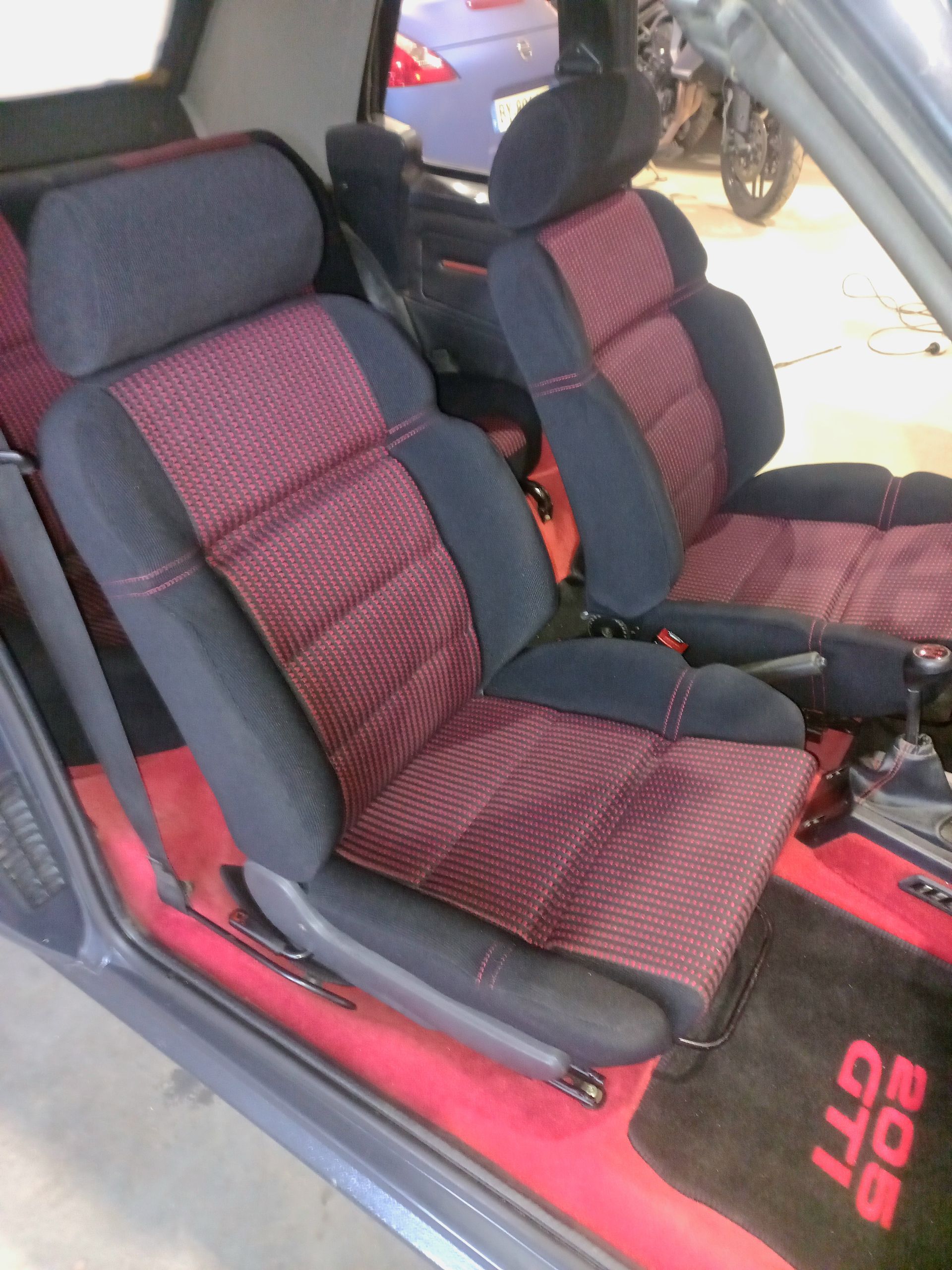 Deux sièges auto rouges et noirs à l'intérieur d'un véhicule, vus depuis la portière ouverte.