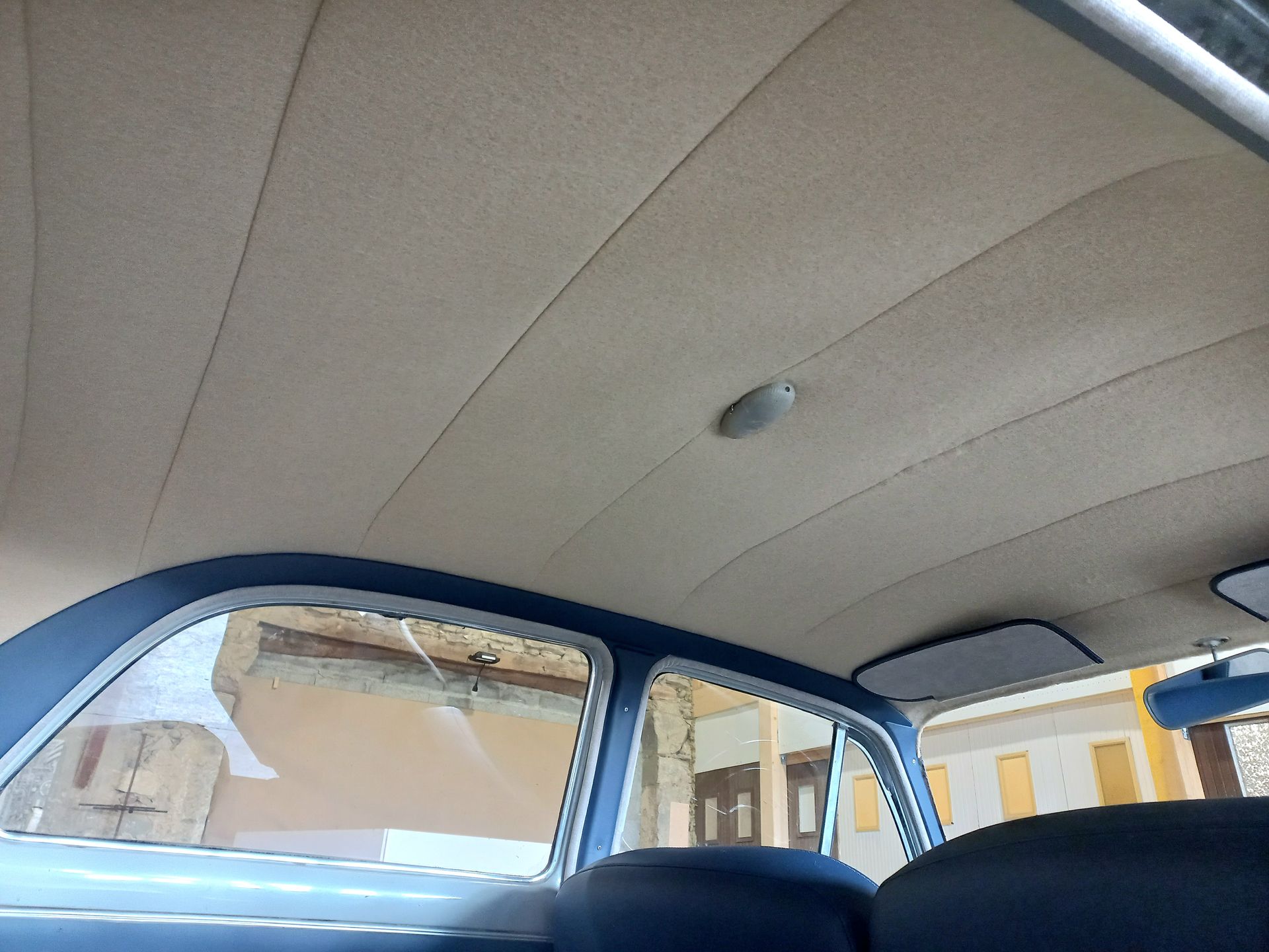 Intérieur d'une voiture ancienne avec plafond beige et encadrement de porte et vitres latérales bleus.