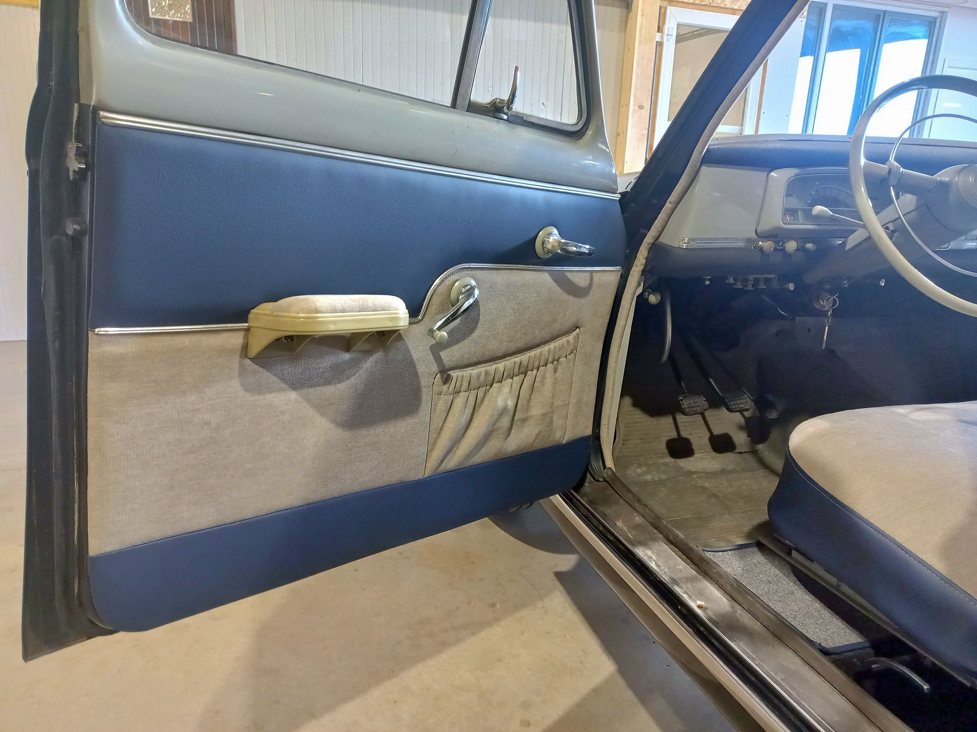 Intérieur d'une voiture ancienne avec porte ouverte, banquette beige et panneau de porte noir et gris dans un garage