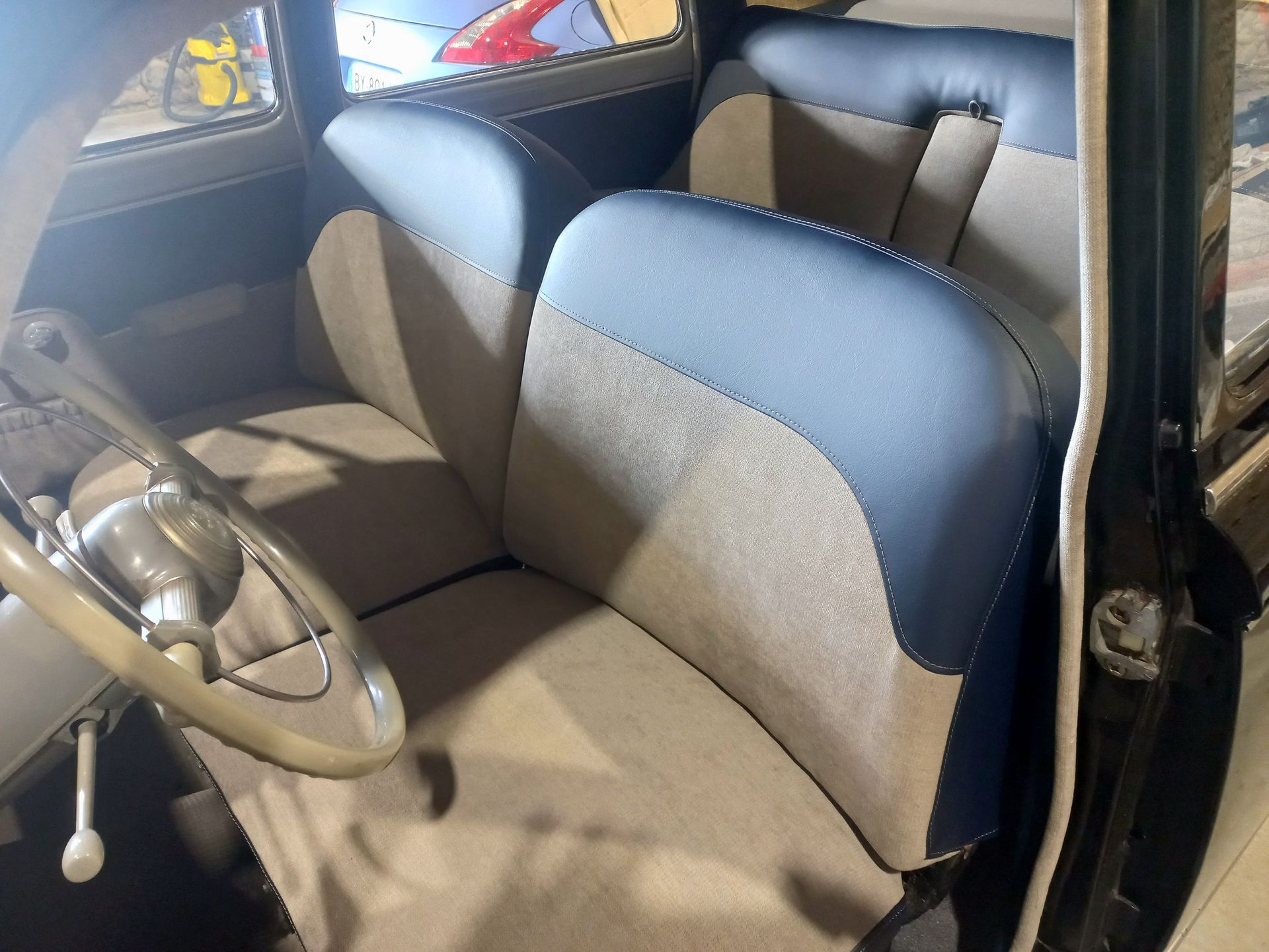 Intérieur d'une voiture ancienne avec banquette et volant noirs et beiges au premier plan