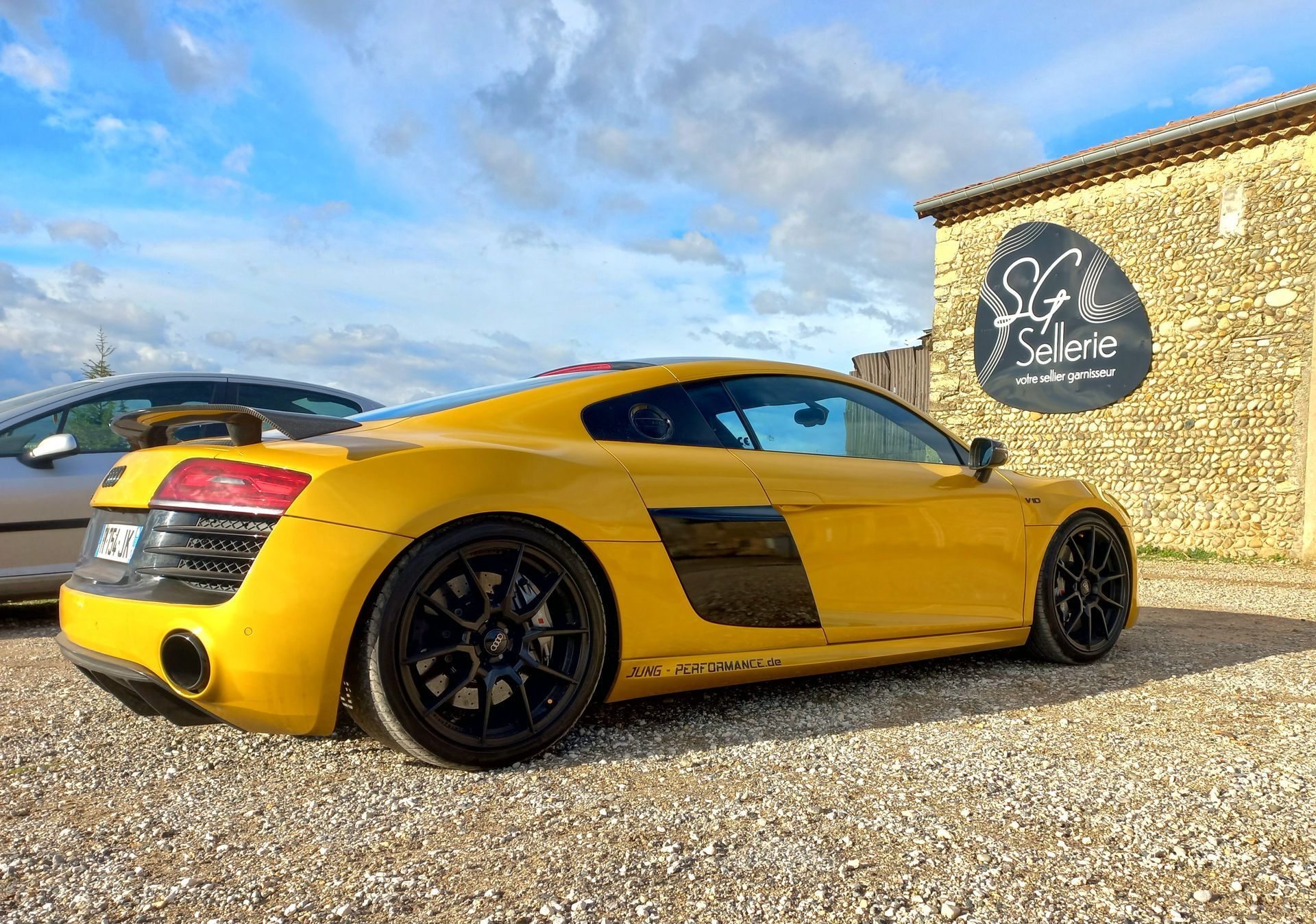 Voiture de sport jaune garée à côté d'un bâtiment en pierre sous un ciel bleu nuageux