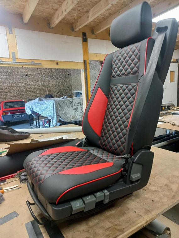 Siège auto inclinable noir et rouge avec appui-tête dans un atelier, posé sur un banc en bois
