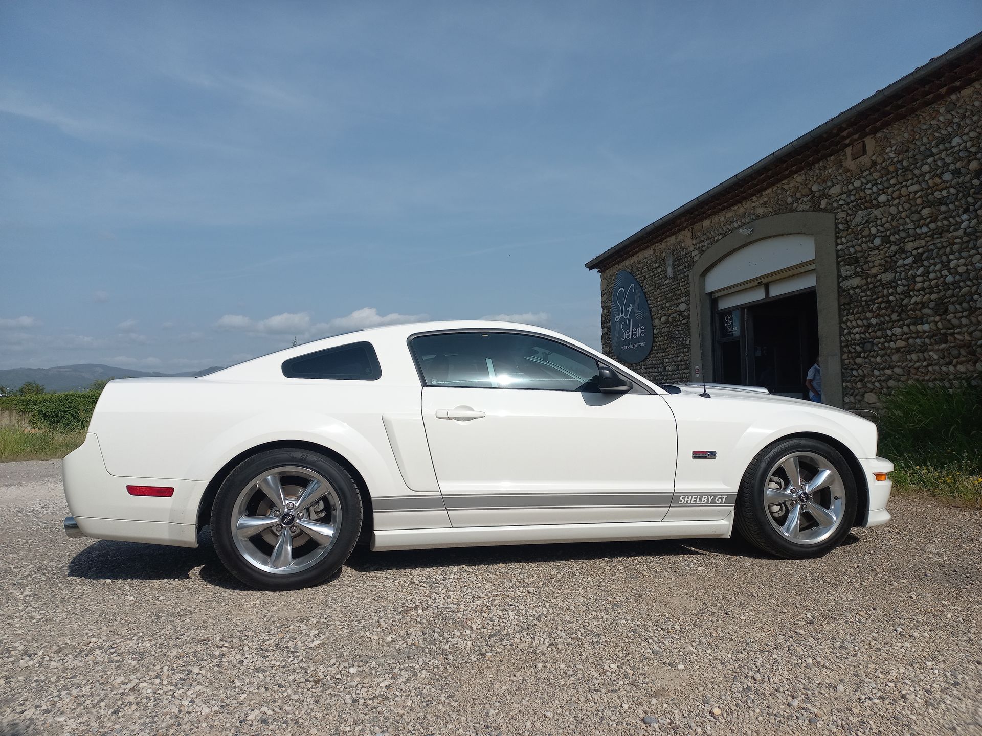 Coupé sport blanc garé sur du gravier à côté d'un bâtiment en pierre sous un ciel bleu
