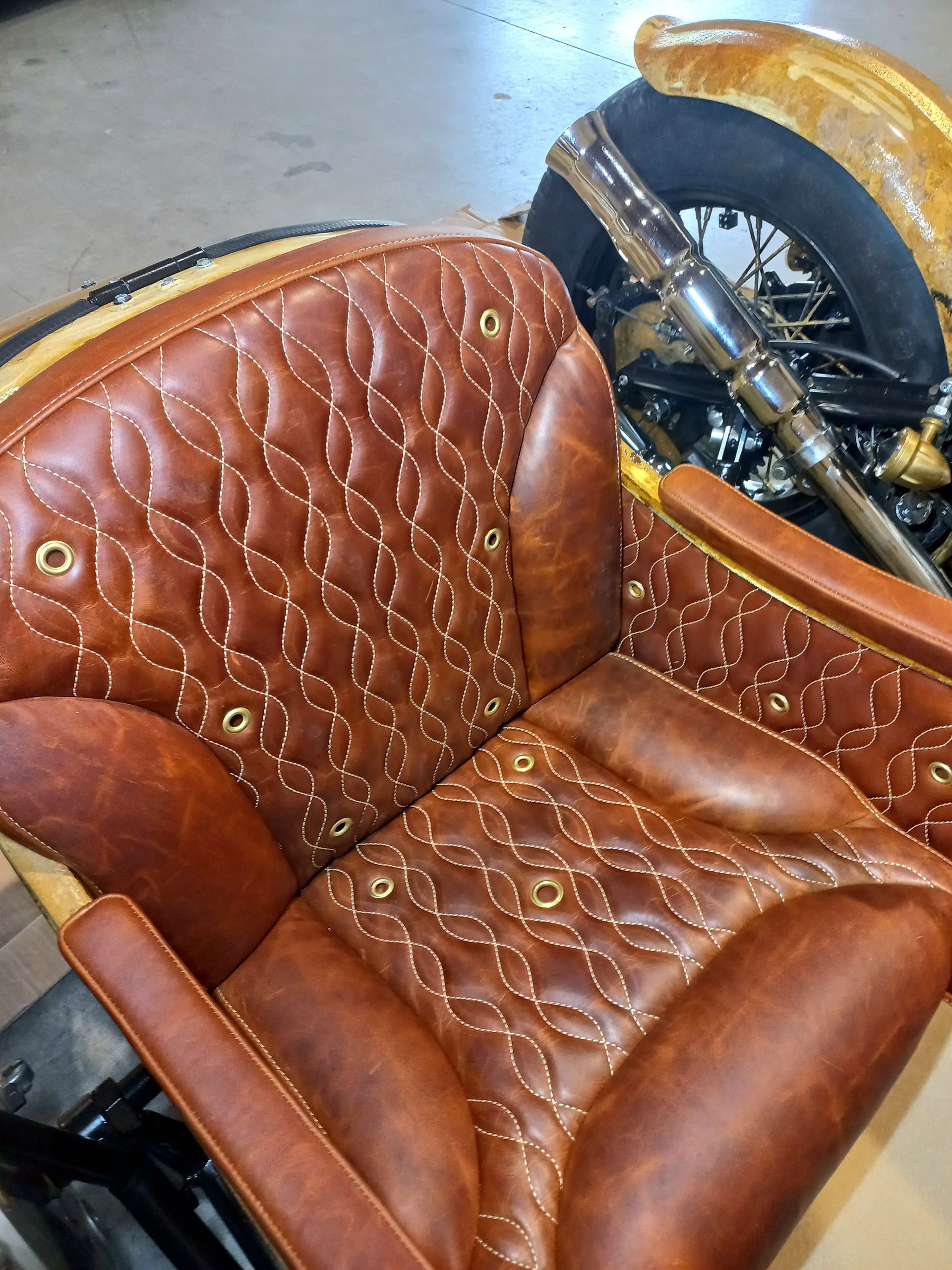 Selle de moto en cuir matelassé marron avec une roue chromée visible en arrière-plan
