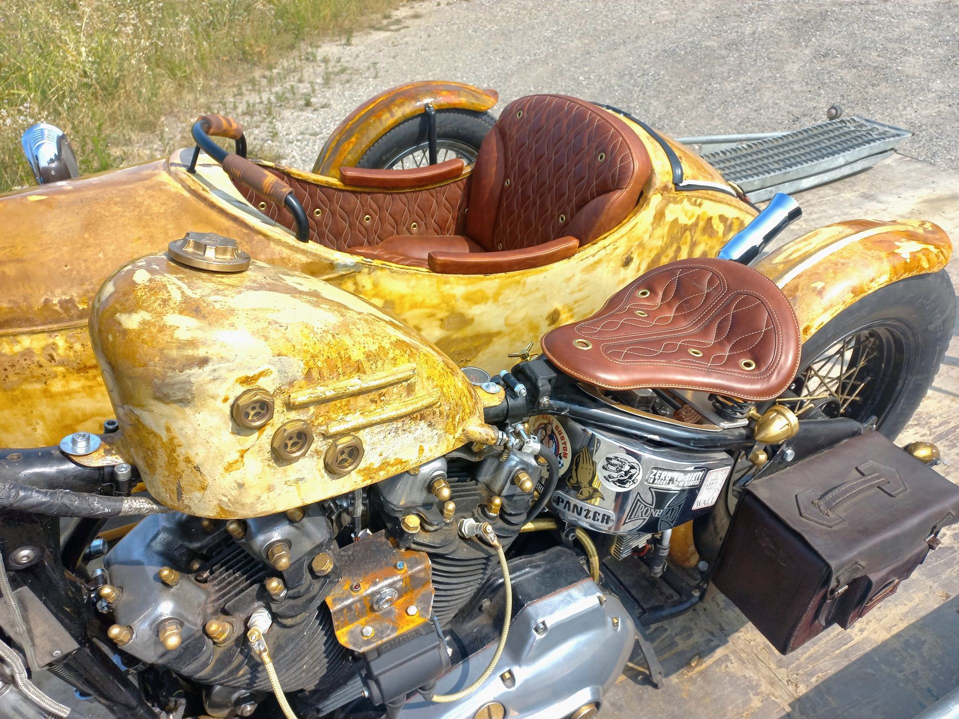 Moto custom jaune avec selle et bagages en cuir marron, garée sur le trottoir.