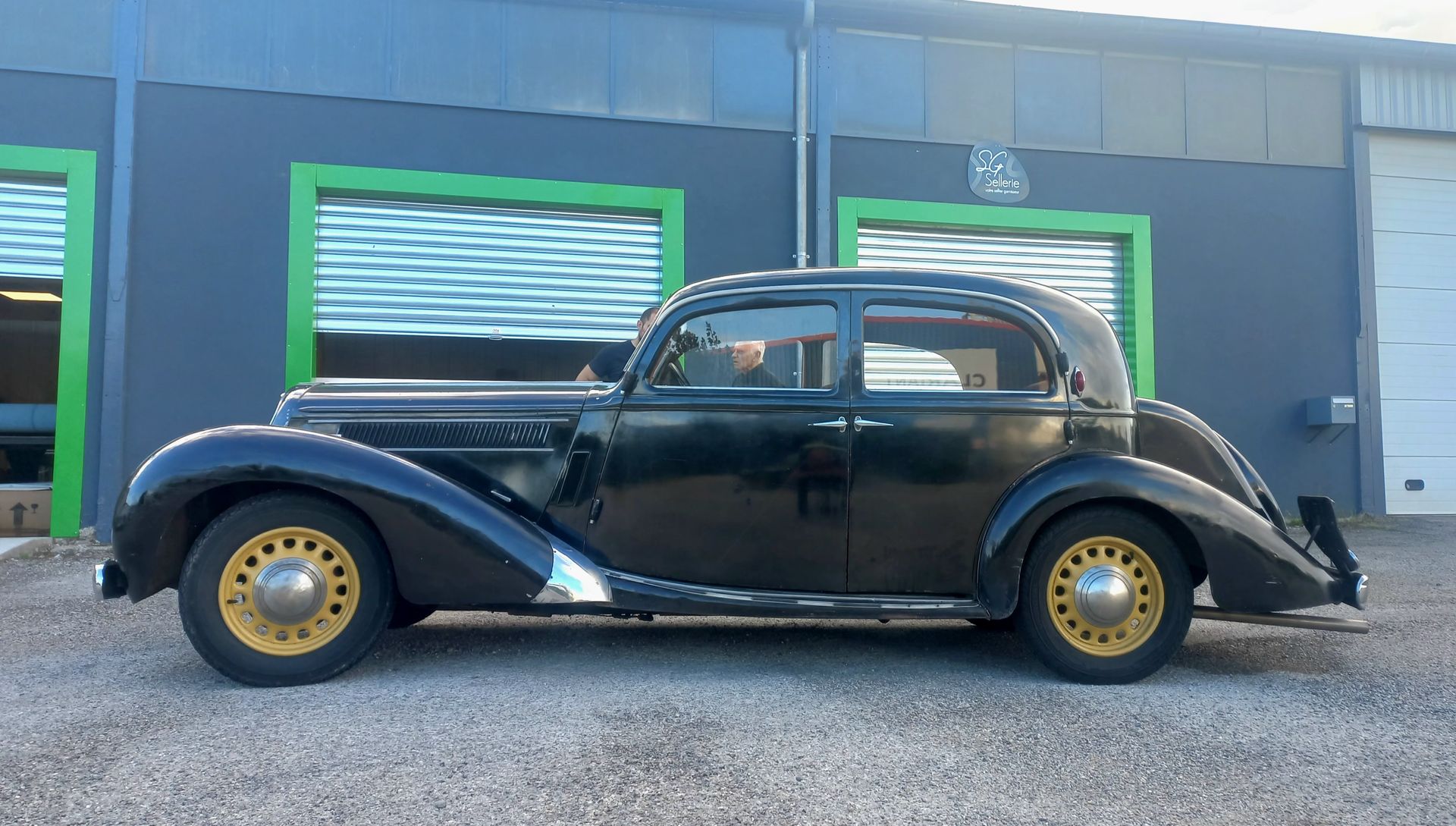 Voiture ancienne noire garée devant un bâtiment aux fenêtres et portes encadrées de vert