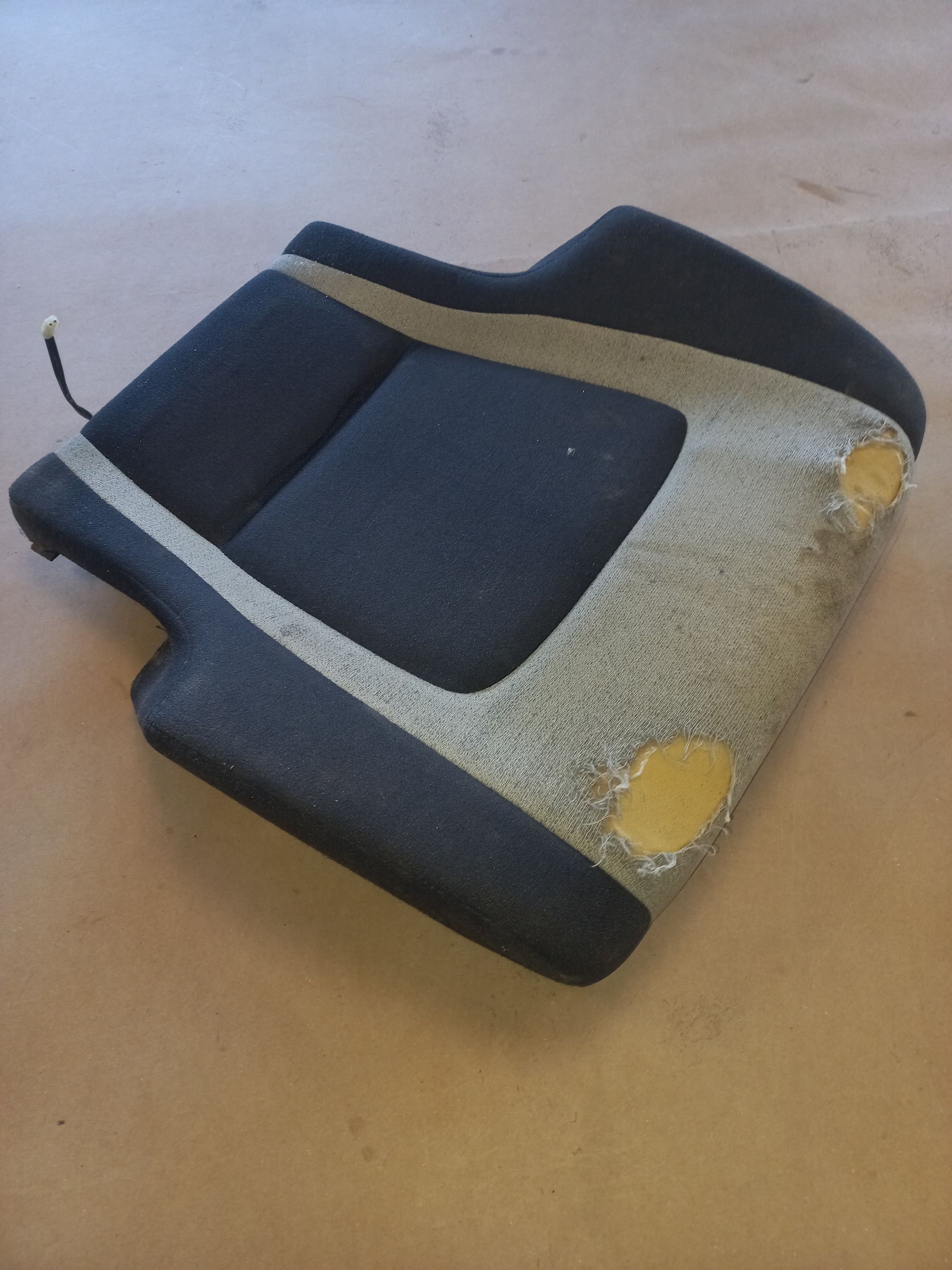 Coussin de chaise gris et noir usé, aux coins jaunis et déchirés, sur un sol beige