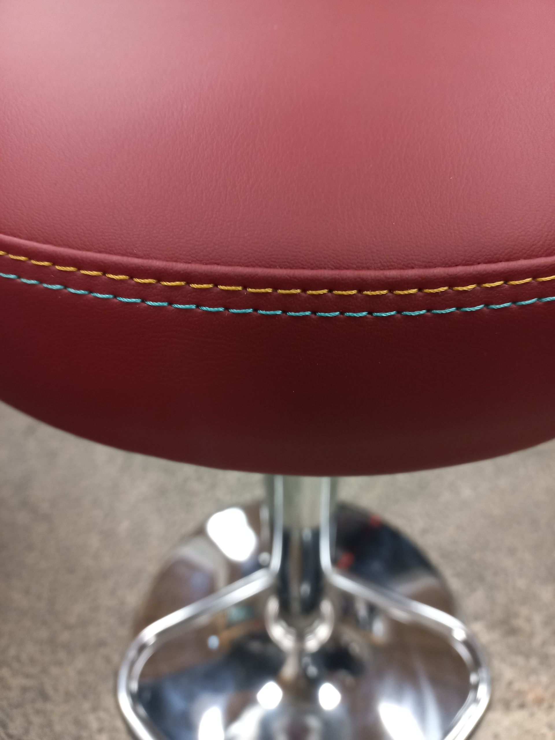 Gros plan sur un tabouret de bar en vinyle bordeaux avec base chromée et coutures apparentes.