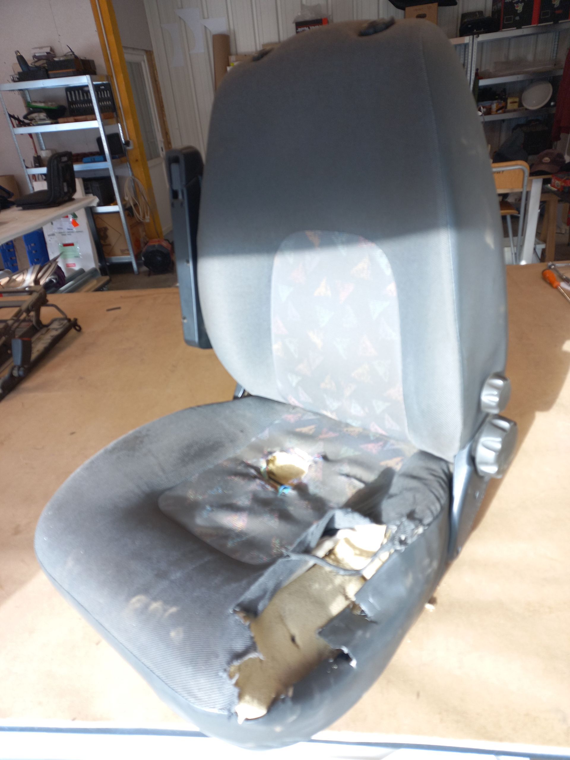Chaise de bureau grise endommagée, avec coussin d'assise déchiré, dans un atelier/garage.