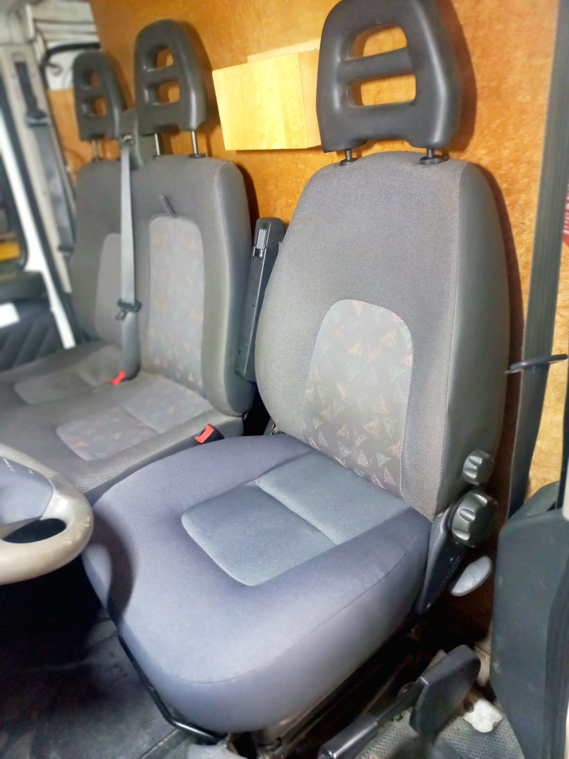 Intérieur d'une voiture avec deux sièges avant gris de style course et un volant visible à gauche.