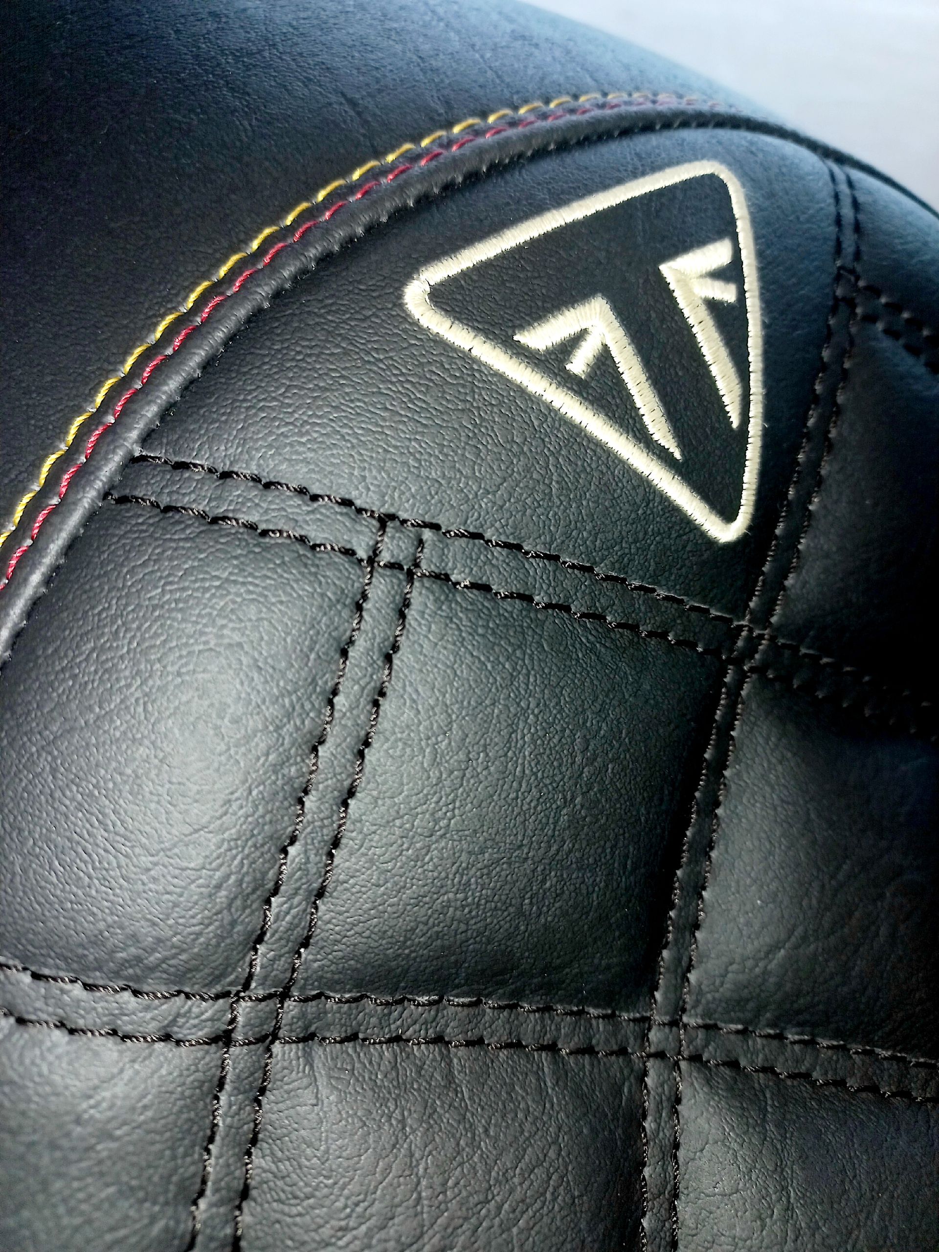 Gros plan sur un siège en cuir matelassé noir avec un logo triangulaire blanc et des surpiqûres arc-en-ciel.