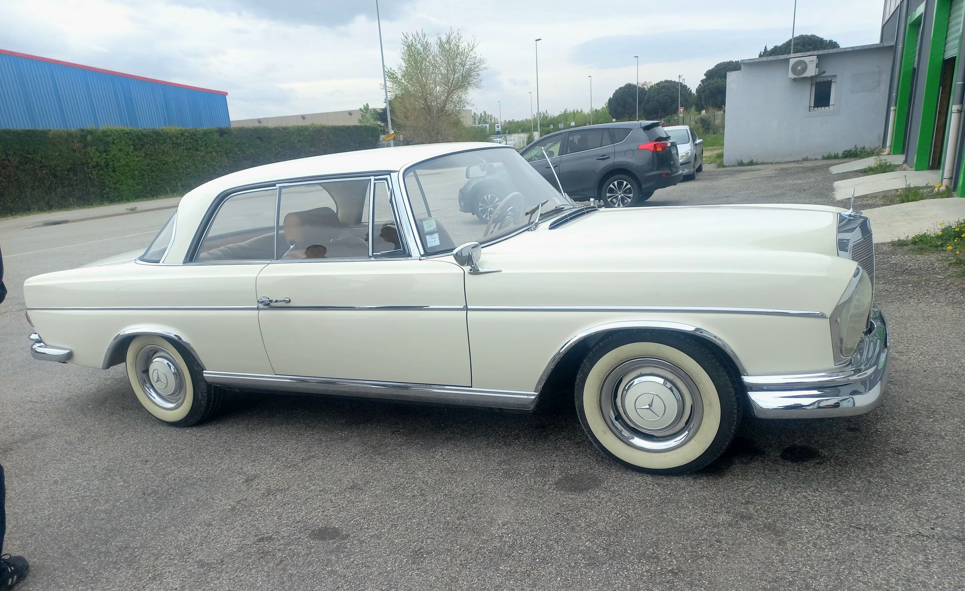 Voiture ancienne classique couleur crème garée à l'extérieur sur un terrain pavé.