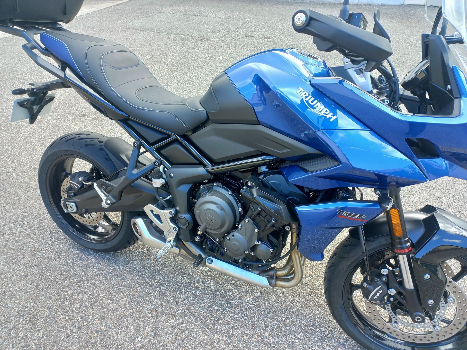 Moto sportive bleue garée sur le trottoir, vue de côté avec selle noire et pot d'échappement chromé.