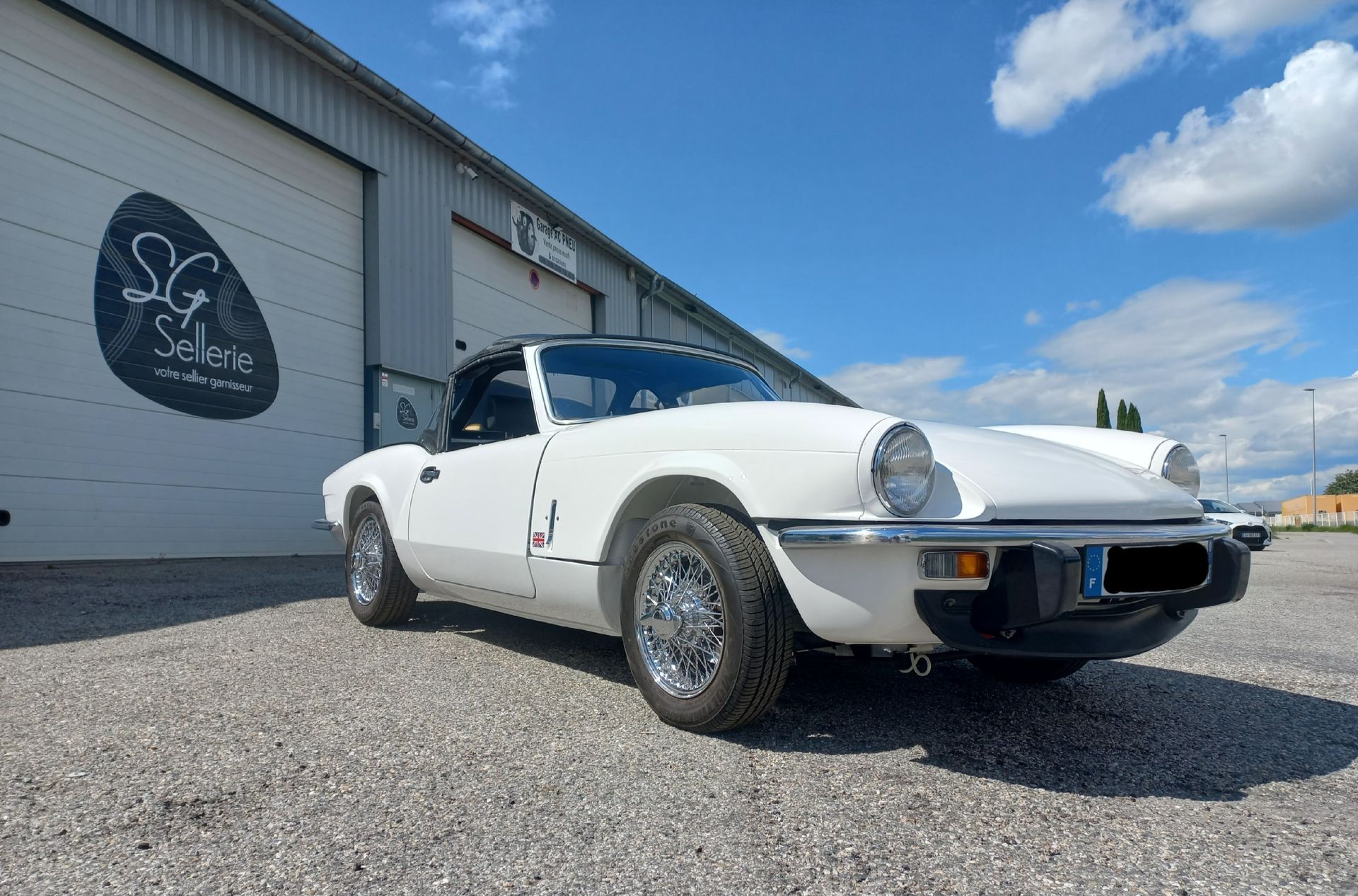 Voiture de sport décapotable blanche classique garée devant un garage sous un ciel bleu