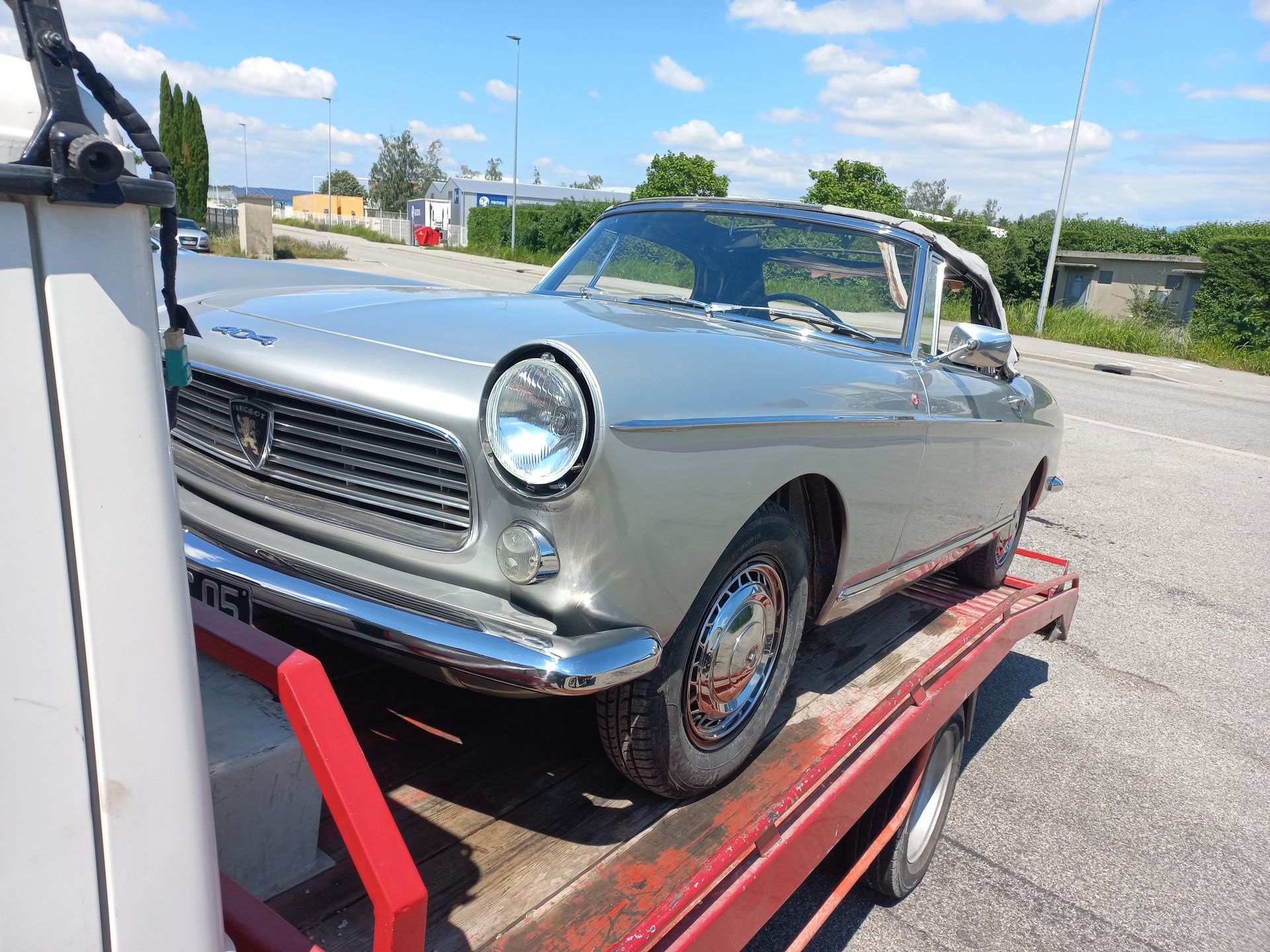 Voiture classique argentée sur une remorque rouge, en plein air sous un ciel bleu ensoleillé