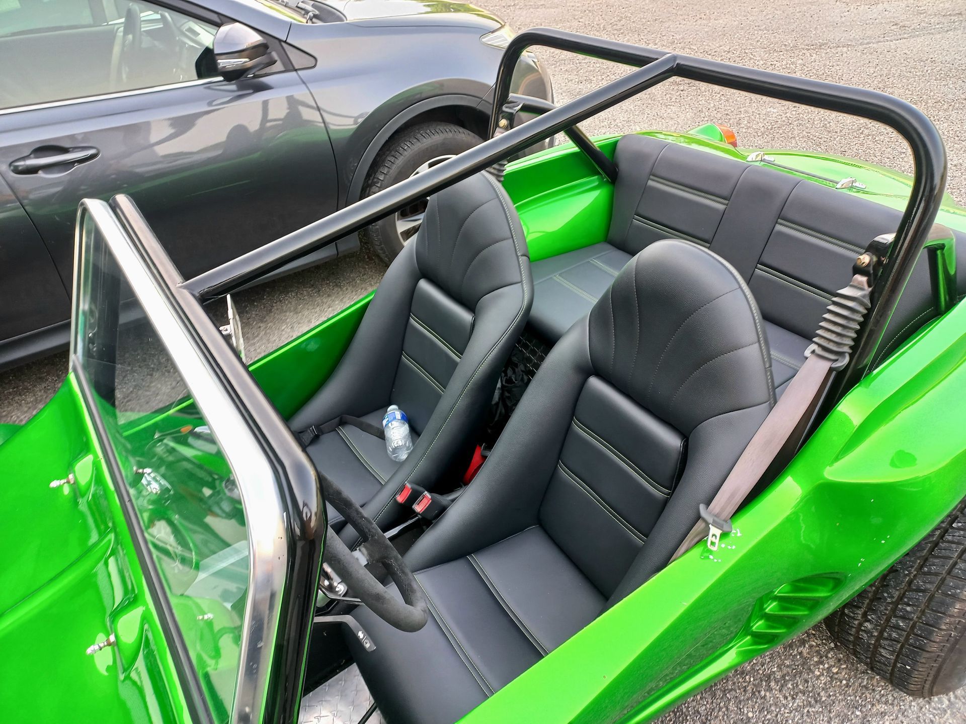 Un buggy vert vif décapotable avec des sièges noirs est garé à côté d'une voiture grise.