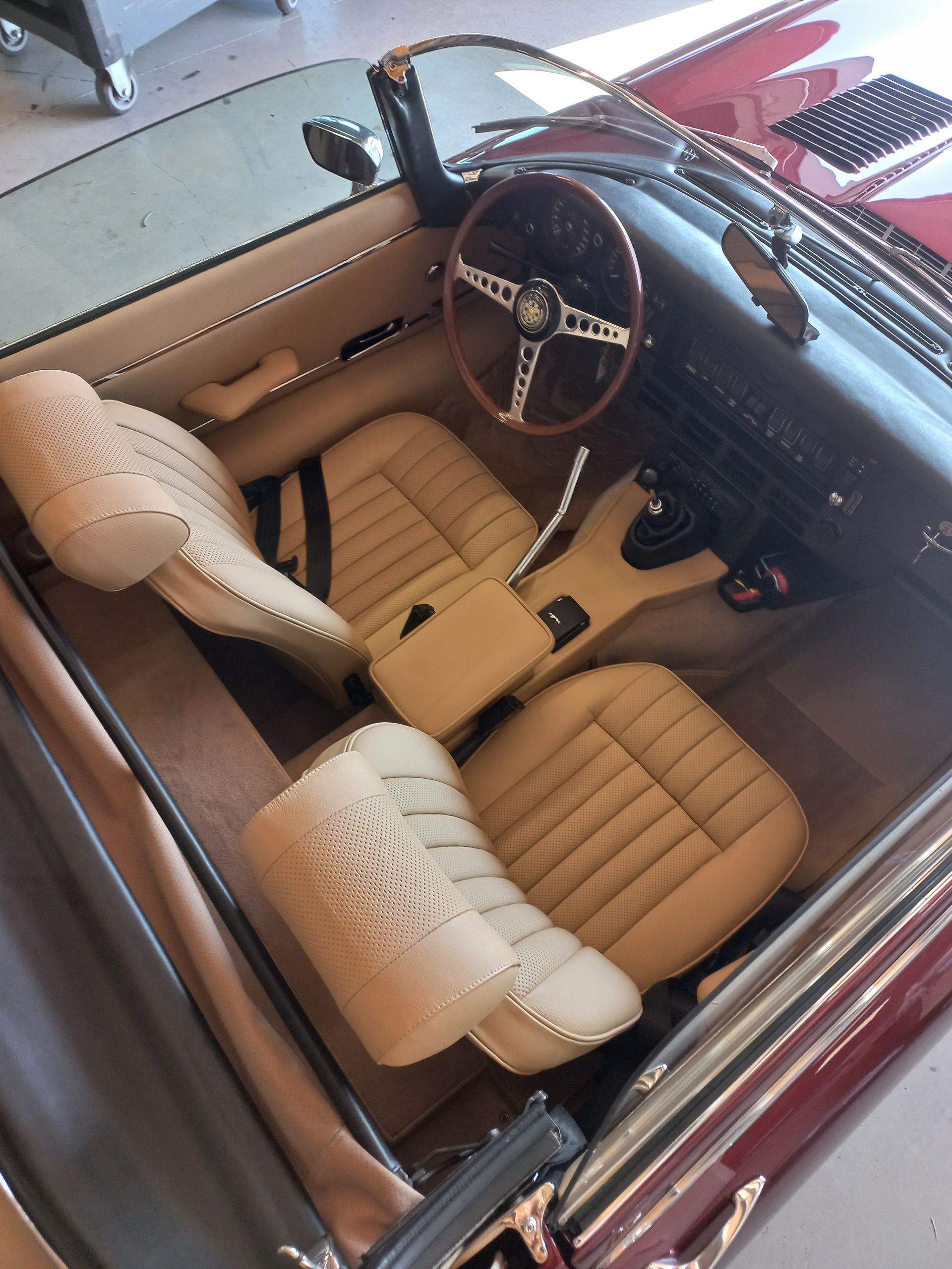 Intérieur de voiture classique avec sièges en cuir beige, volant en bois et tableau de bord bordeaux.