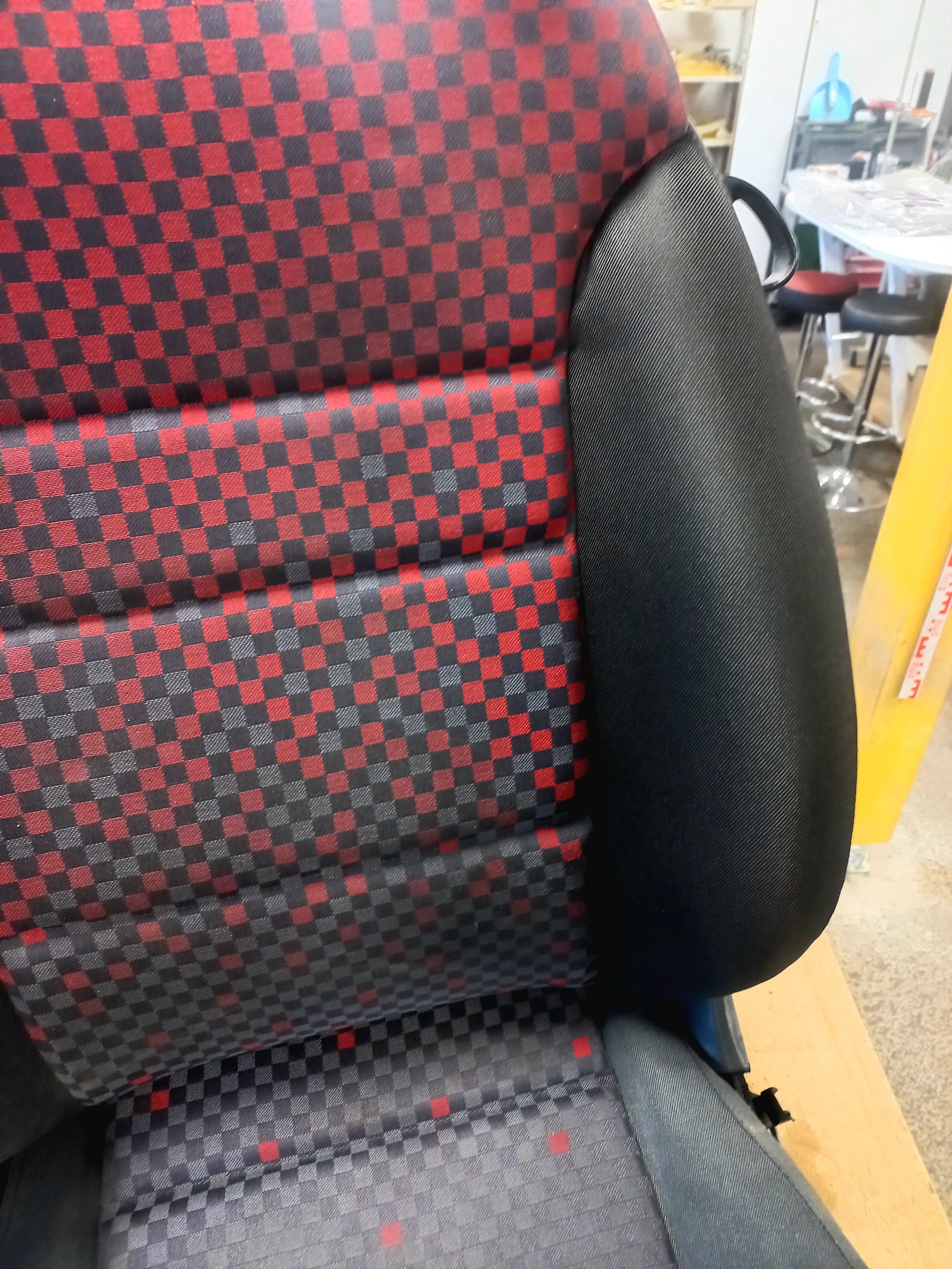 Gros plan sur un siège auto à carreaux rouges et noirs avec des renforts latéraux gris.