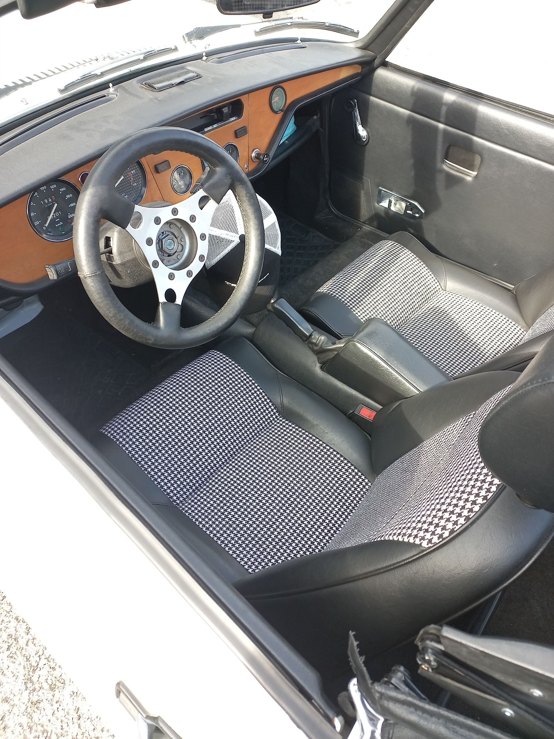 Intérieur de voiture classique avec sièges noirs et gris, tableau de bord en bois et volant argenté