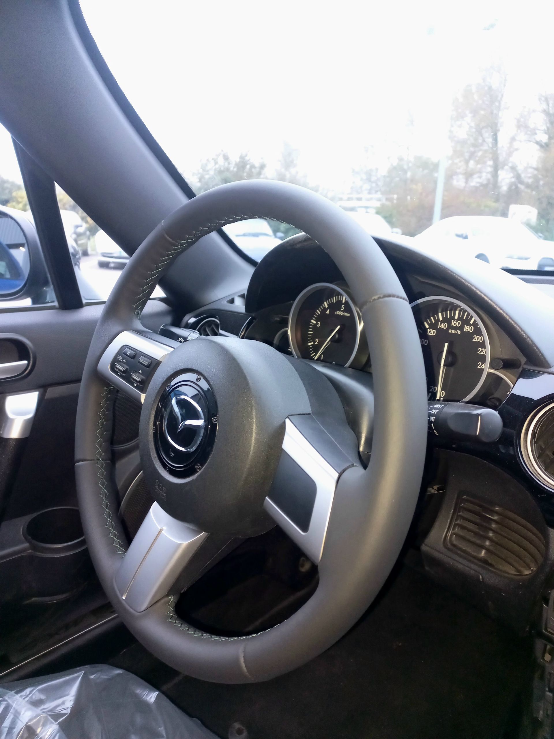 Gros plan sur le volant et le tableau de bord d'une Mazda, à l'intérieur d'une voiture, vus du siège conducteur.