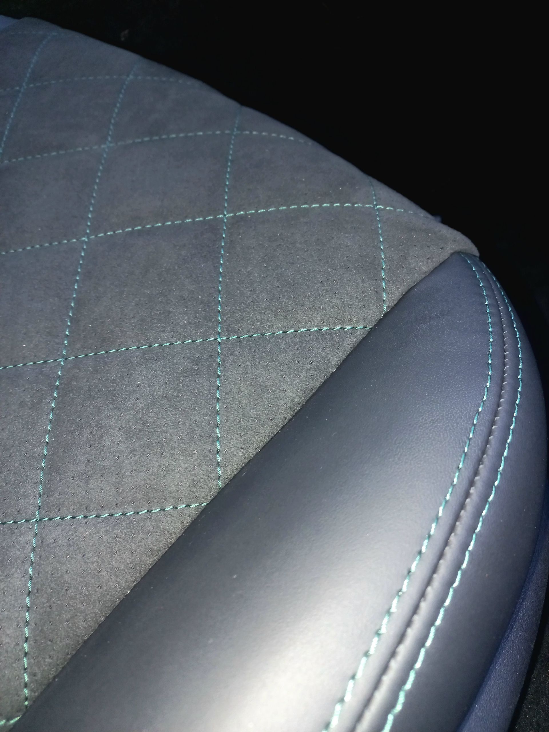 Gros plan sur un siège auto gris matelassé avec des surpiqûres bleues et un bord en cuir noir