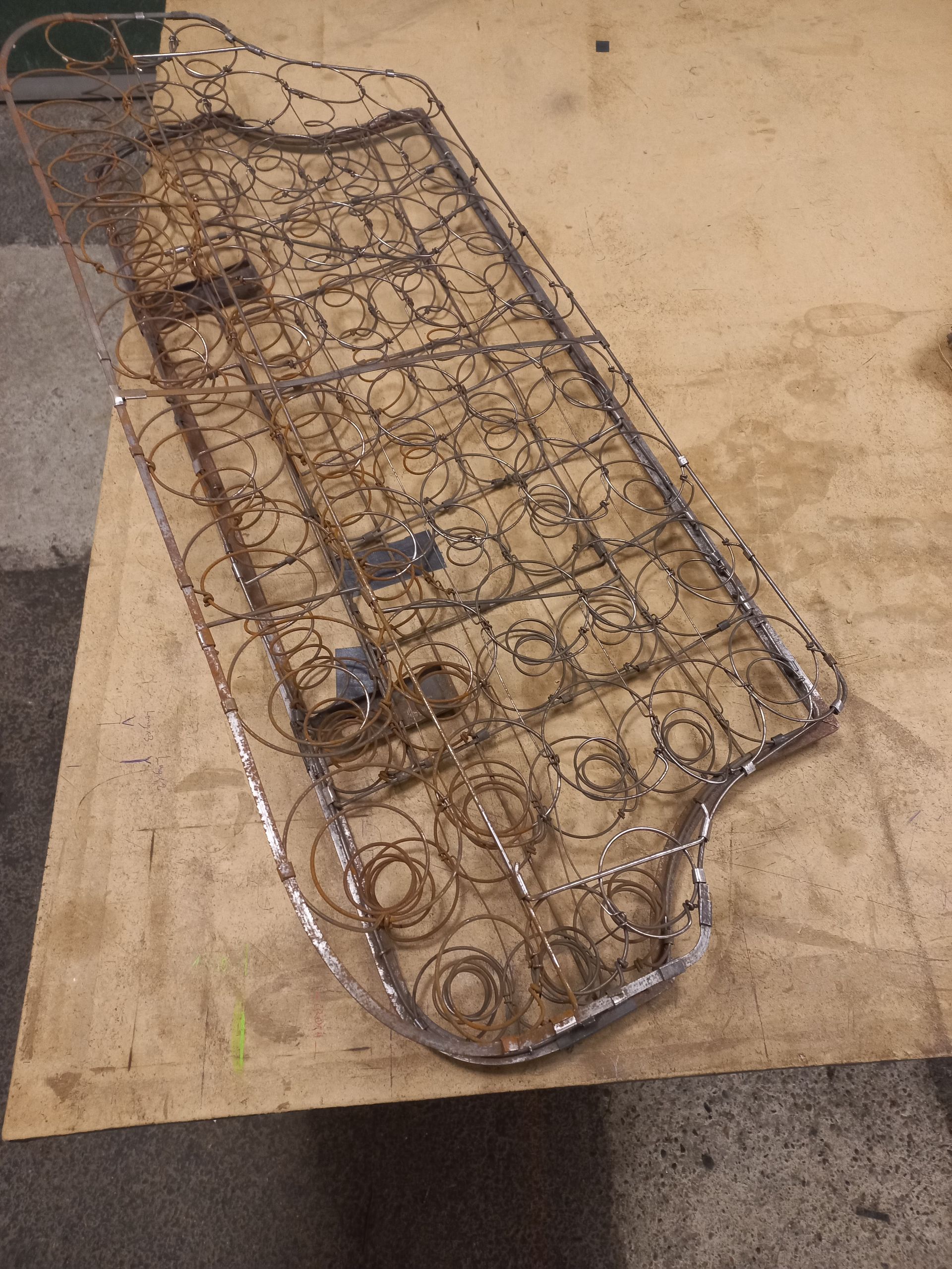 Un vieux coussin de canapé, aux ressorts apparents et au tissu déchiré, posé sur un établi en bois.